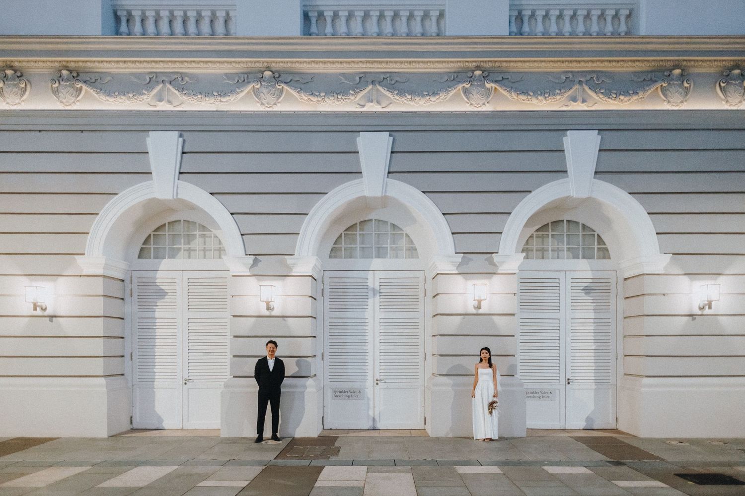 Elegant couple photoshoot against a classical white architectural backdrop with arches.