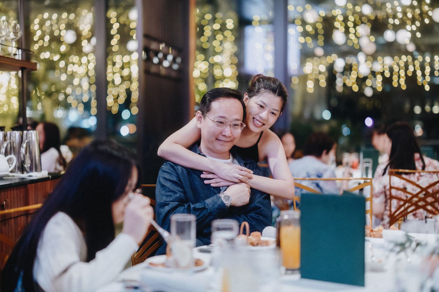 Group of wedding guests mingling during a reception in an elegant room decorated with sparkling string lights and greenery.