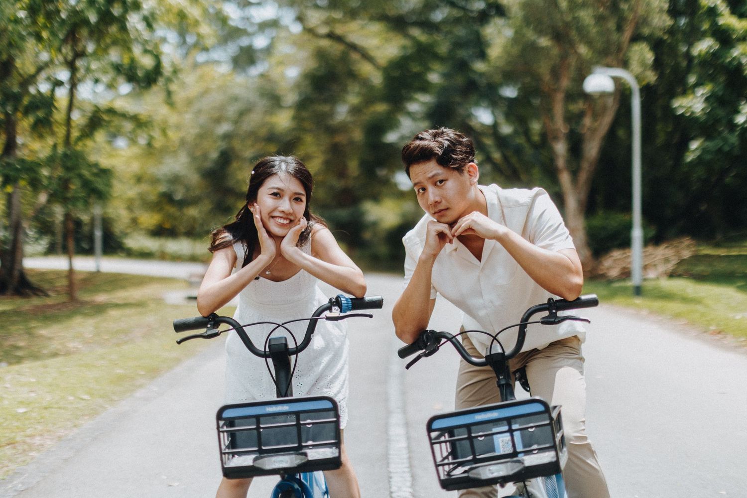 Couple riding bicycles together on a tree-lined path during a summer photoshoot.