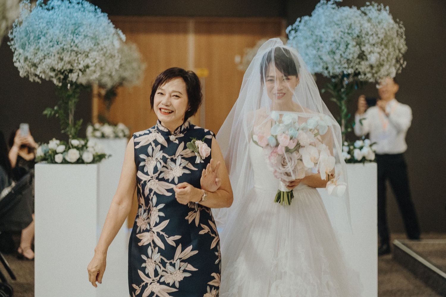 Wedding guests in floral navy dresses and white bouquets stand alongside bride in traditional white gown.