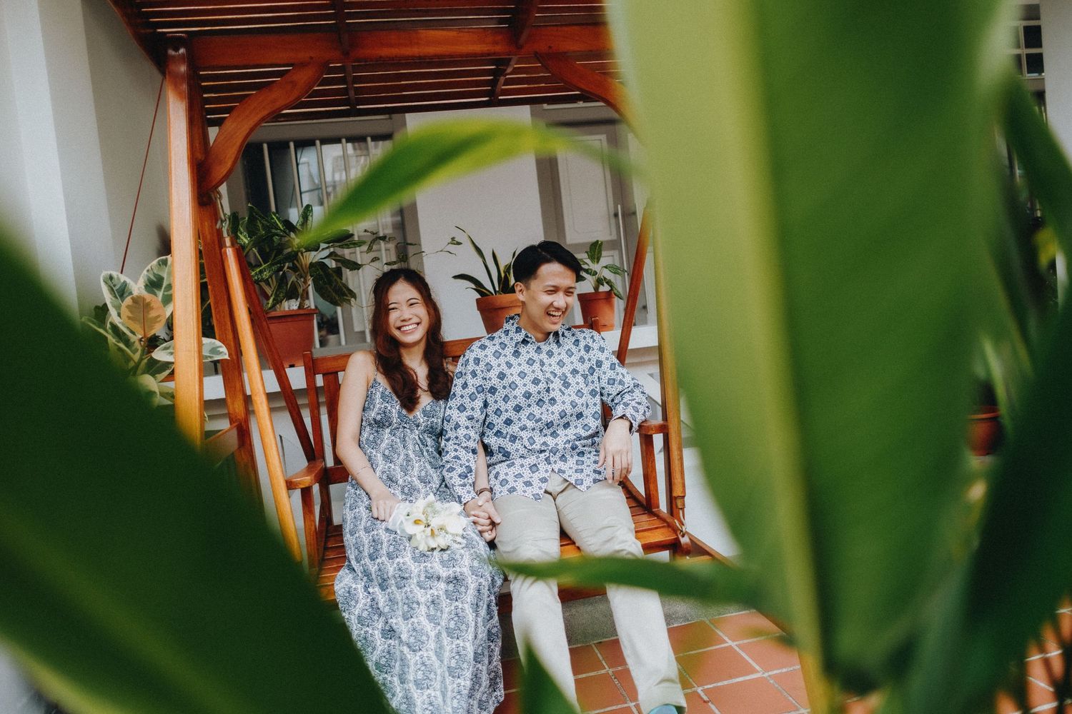 Couple sitting together on a patio surrounded by lush green plants in an outdoor setting.
