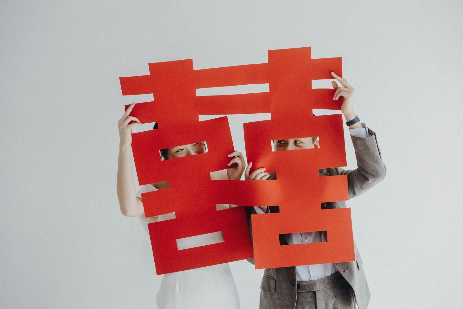 Person holding red Chinese double happiness character symbol against white wall.