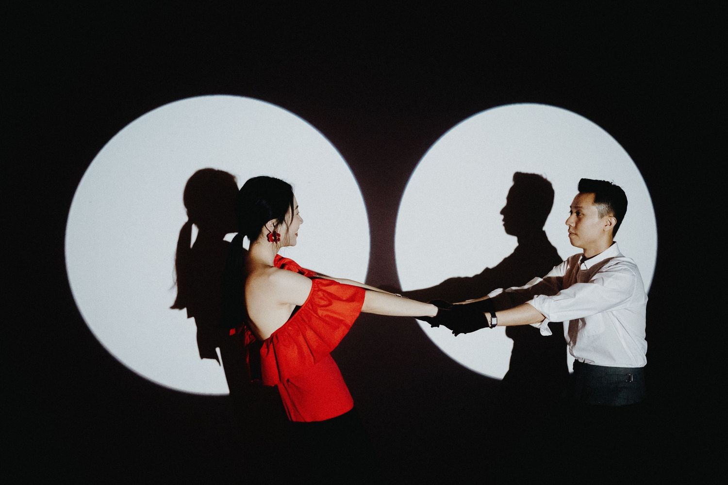 Creative silhouette photo of people dancing in two spotlit circles, with figures in red and black against white light.