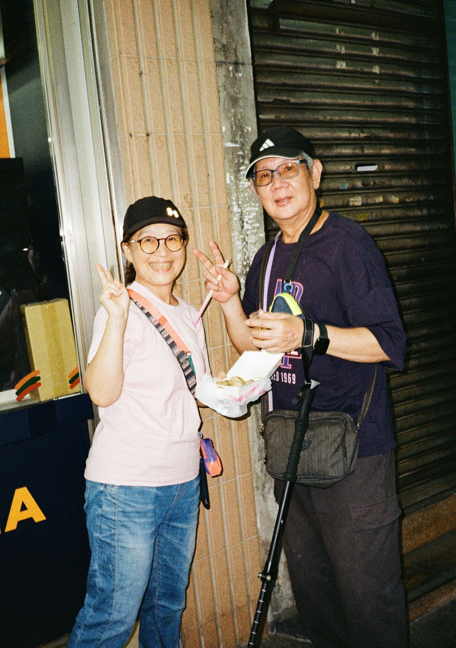 Friends posing together at night in casual outfits making peace signs outside a storefront.