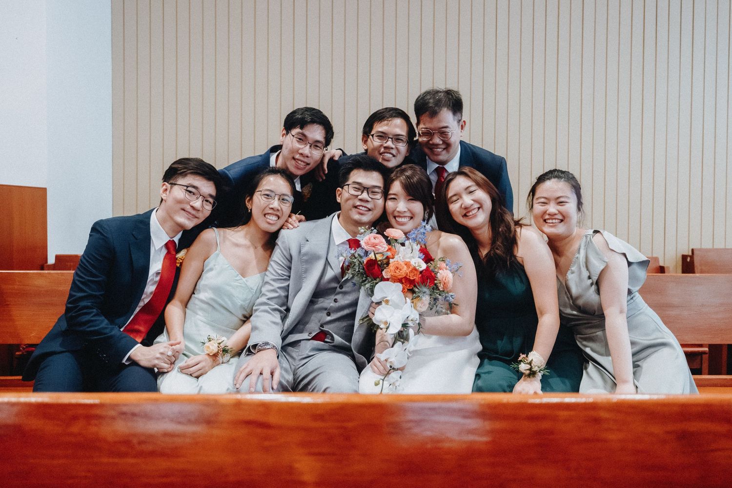 Group wedding photo showing joyful celebration on wooden church pews.