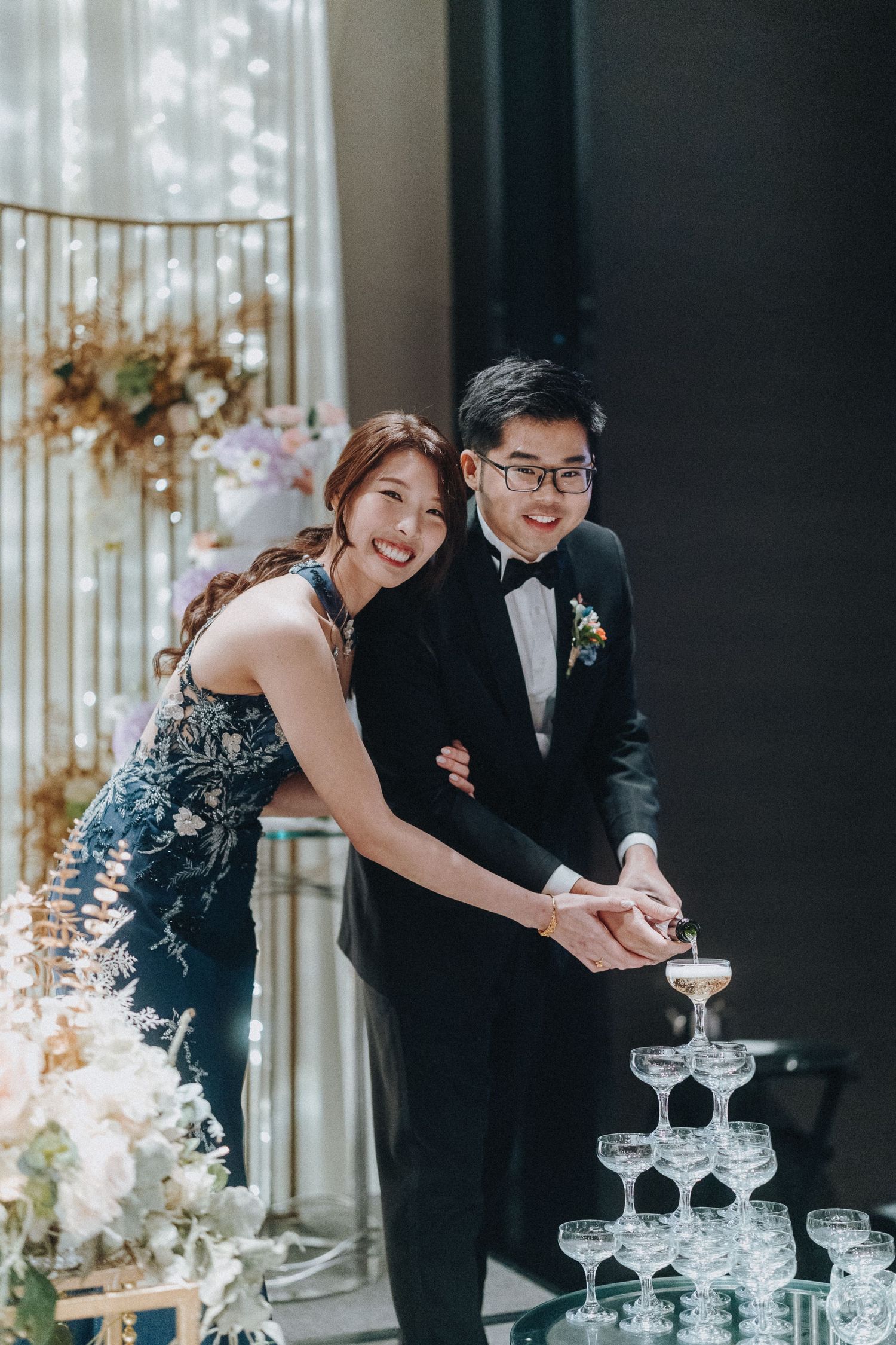 A couple pours champagne into a tower of glasses at their elegant wedding reception.