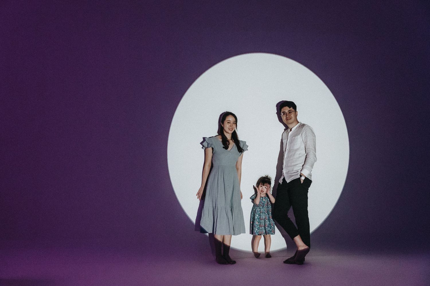 Family portrait against purple background with dramatic circular white spotlight.