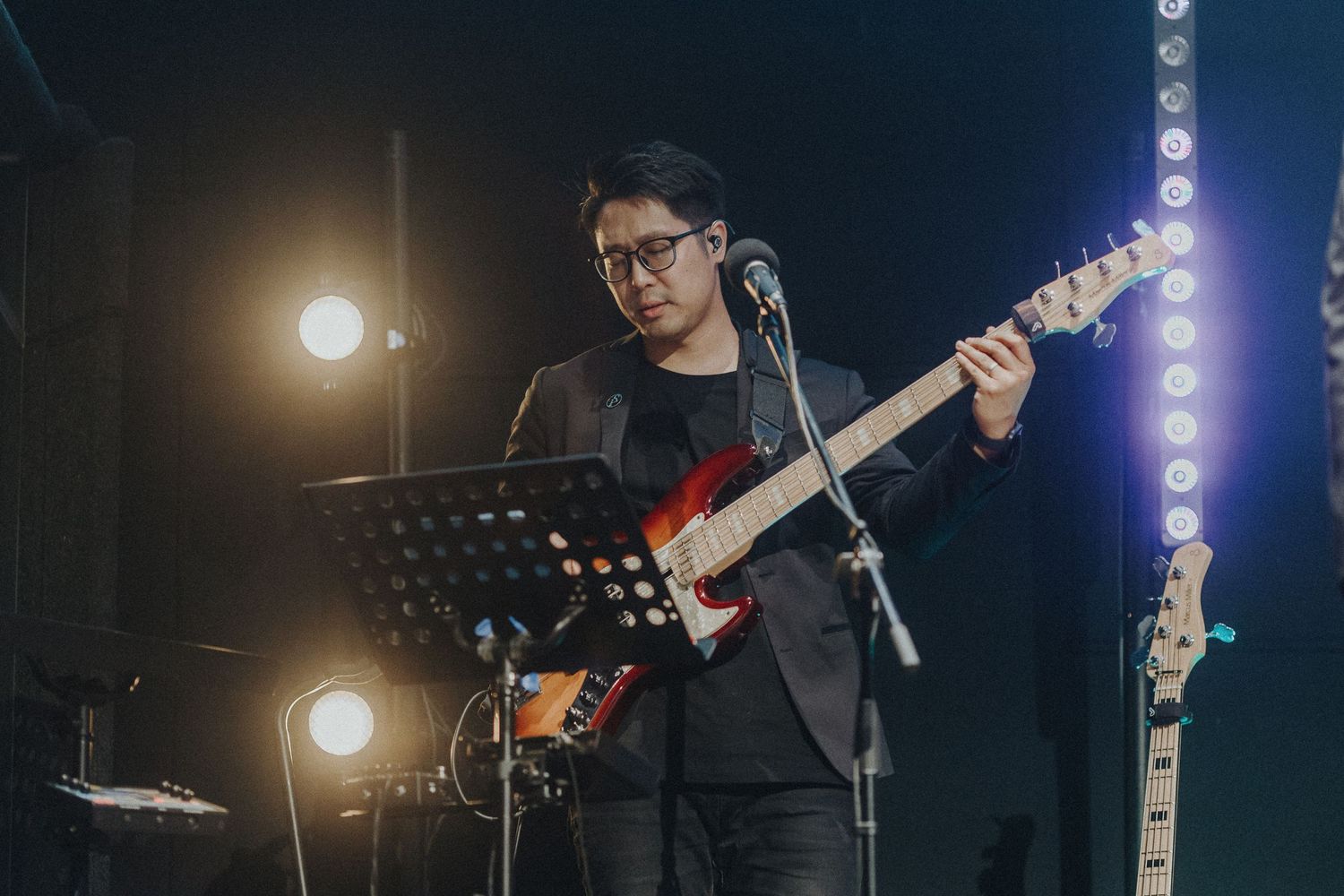 Musicians performing on dimly lit concert stage with spotlights and dramatic lighting effects.