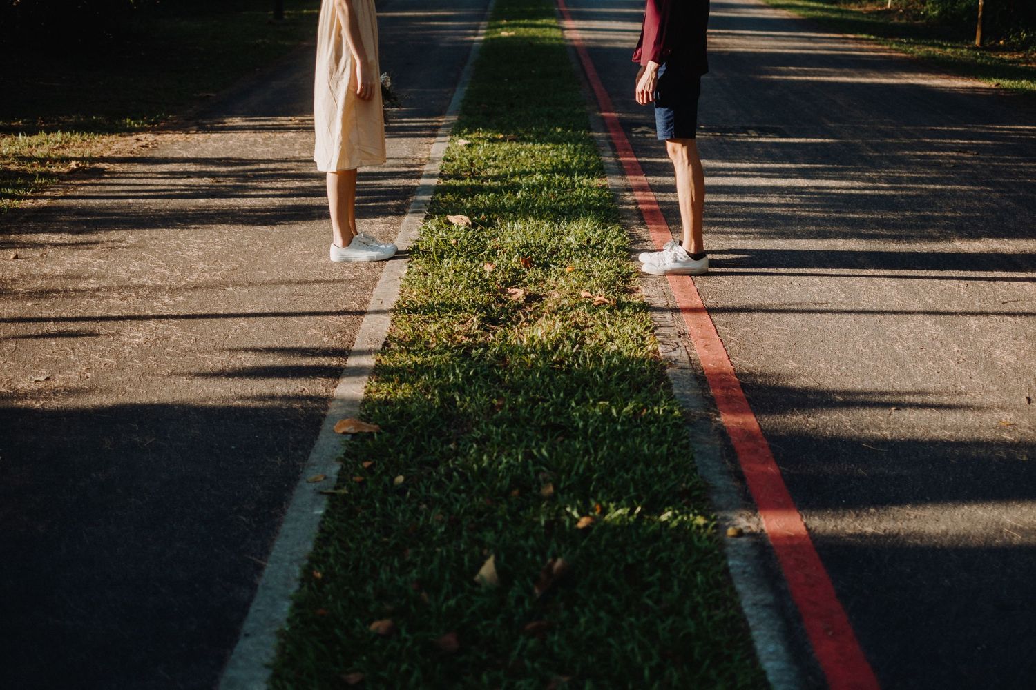 Two people's legs casting long shadows on a red-lined path in golden sunlight.