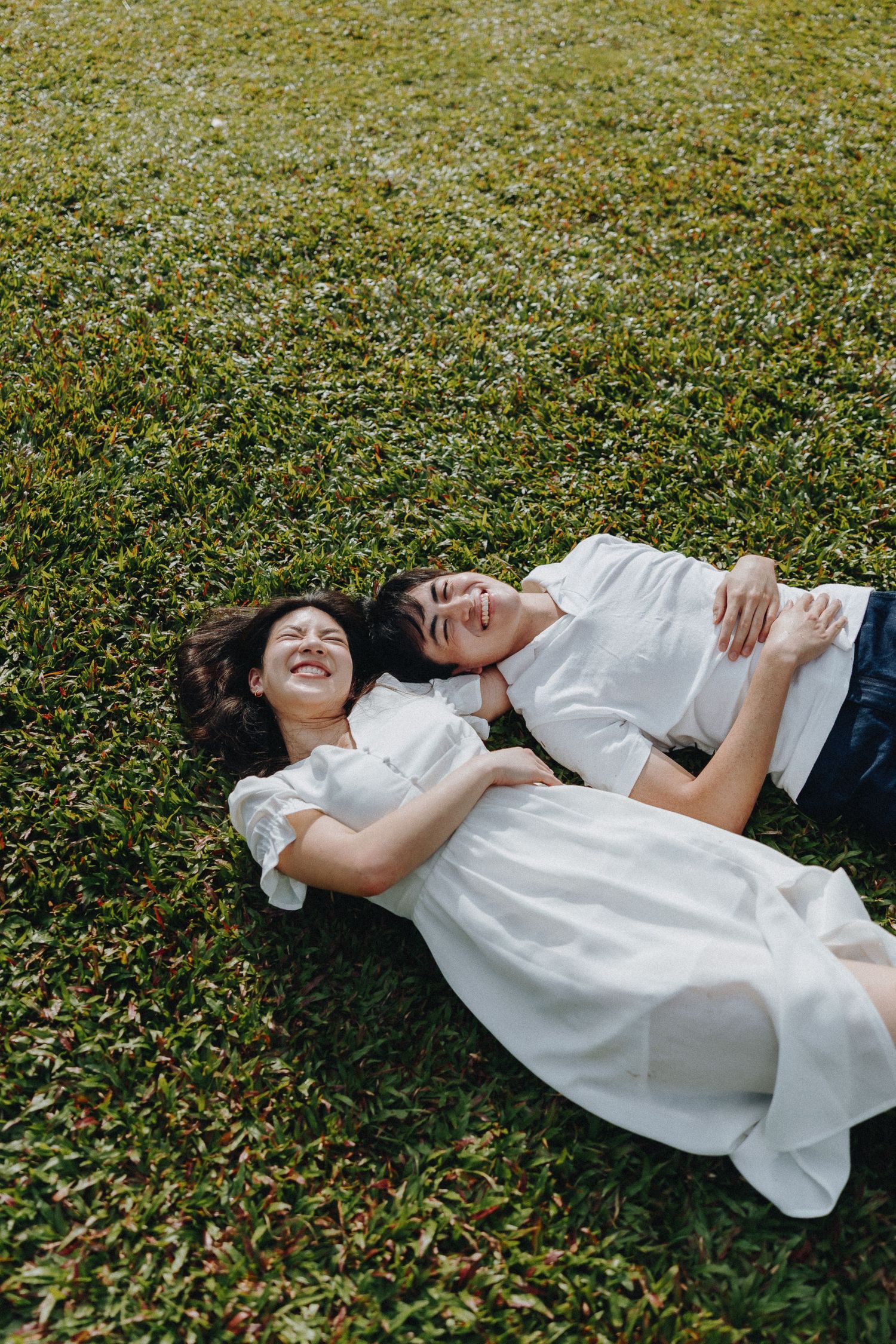 A candid moment of joy captured as a couple lies on grass together.
