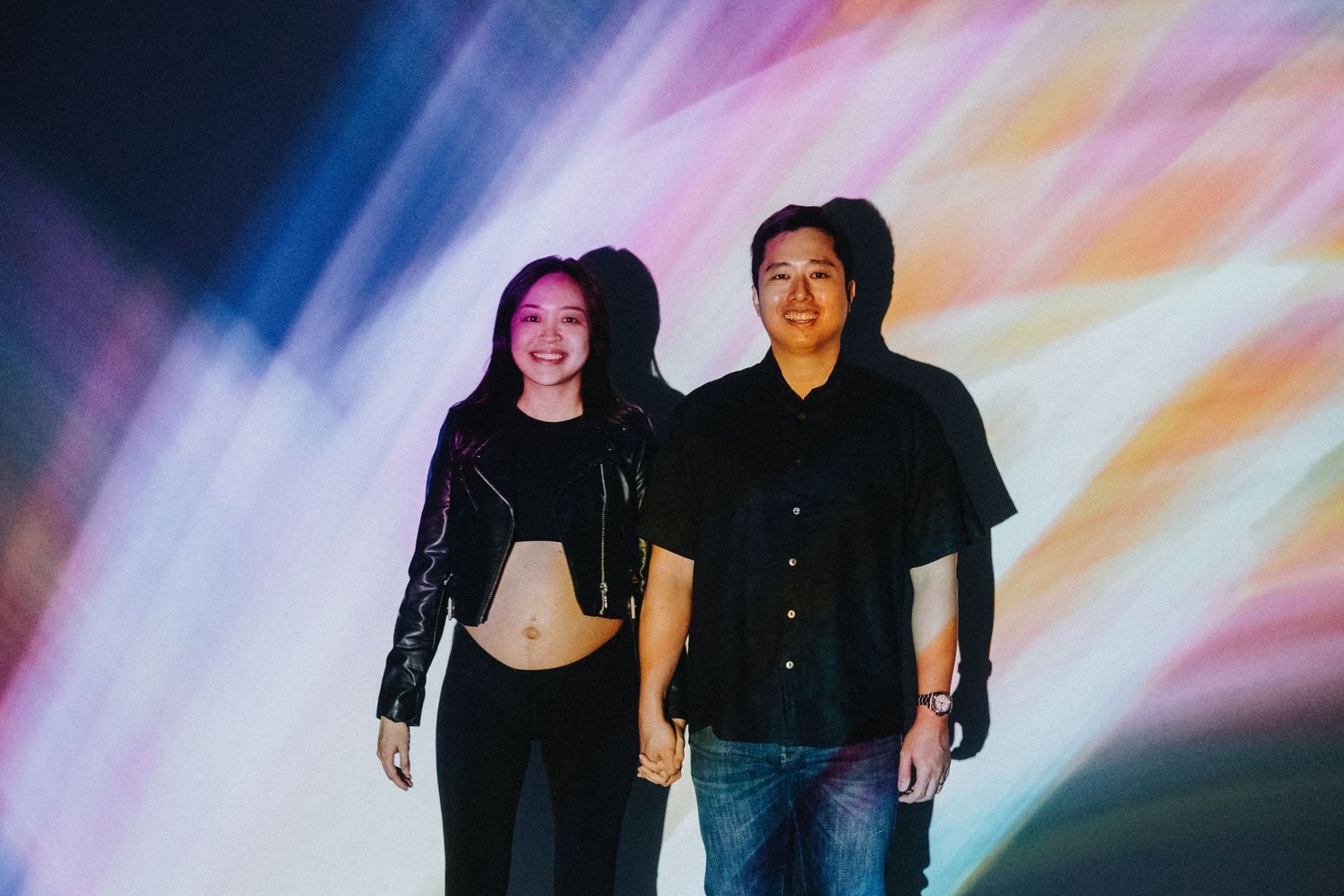 Couple posing against a vibrant colorful background with neon lights and rainbow effects.