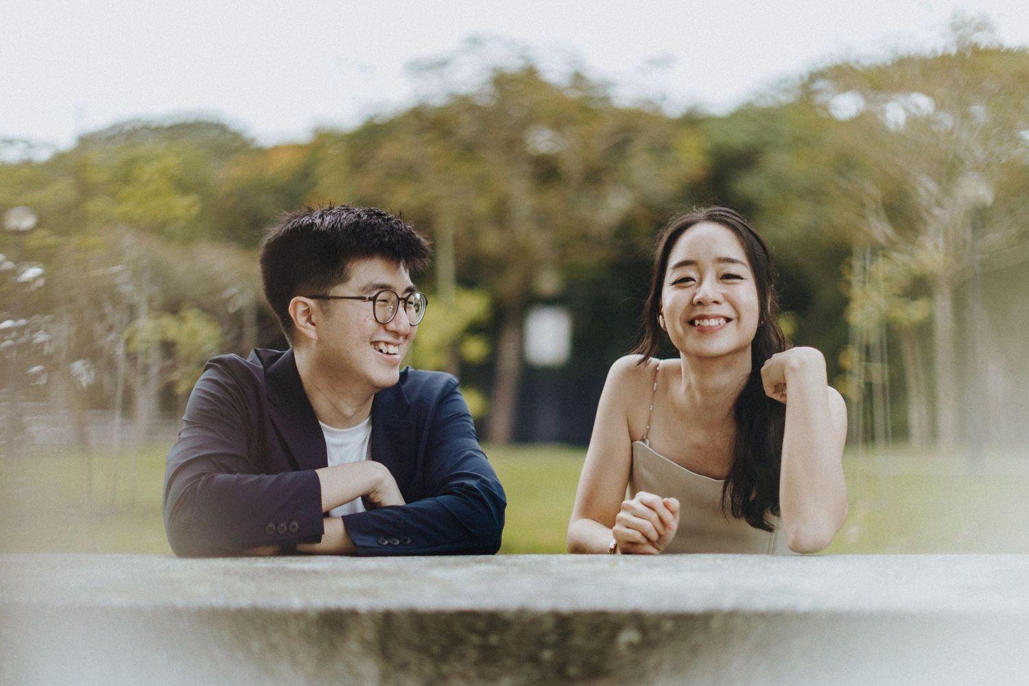 A couple shares a joyful moment while lying on grass together in a park setting.