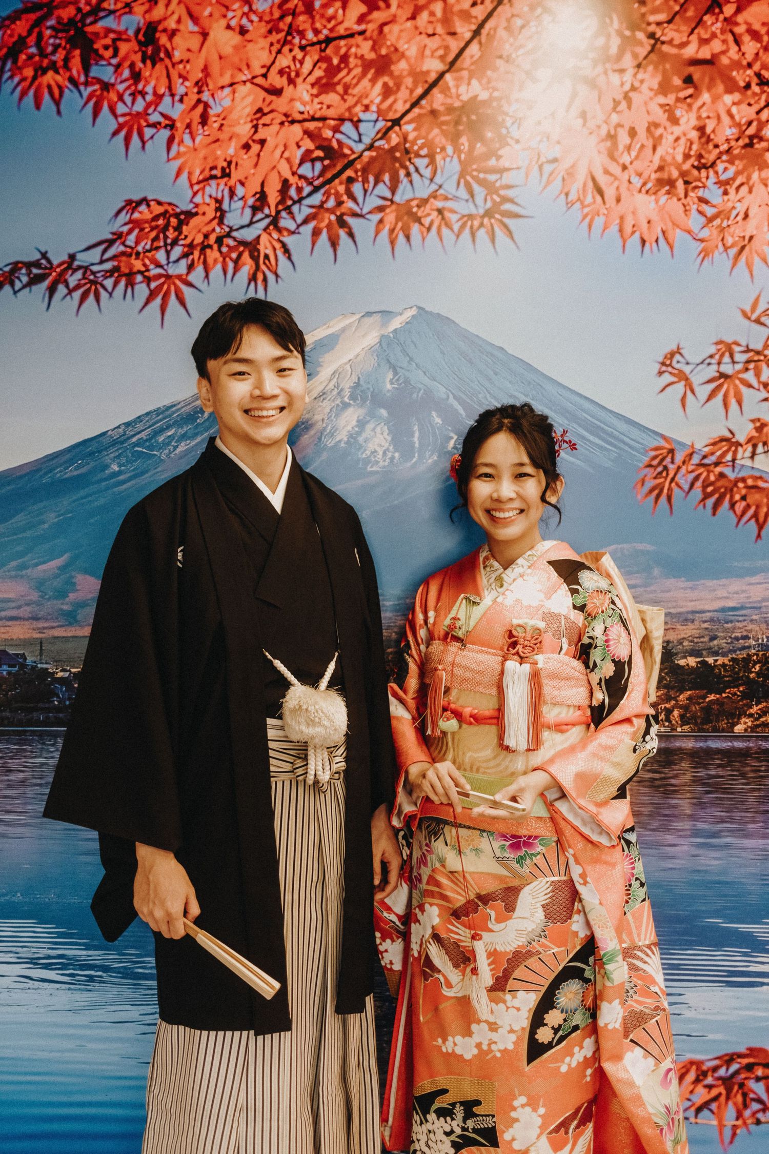Traditional Japanese wedding couple poses against Mount Fuji with vibrant red maple leaves framing the scene.
