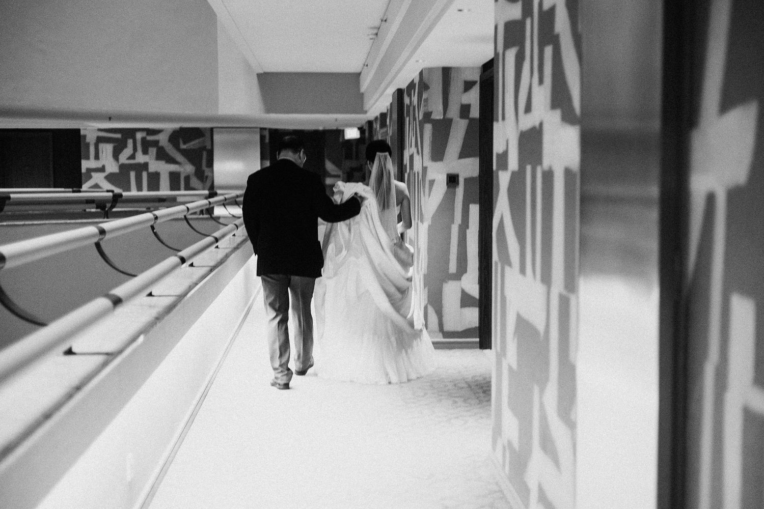 Long corridor with mirrored walls and wedding party members walking.
