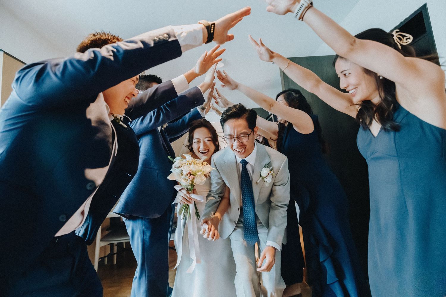 Wedding party forming an archway tunnel with their arms raised in celebration.