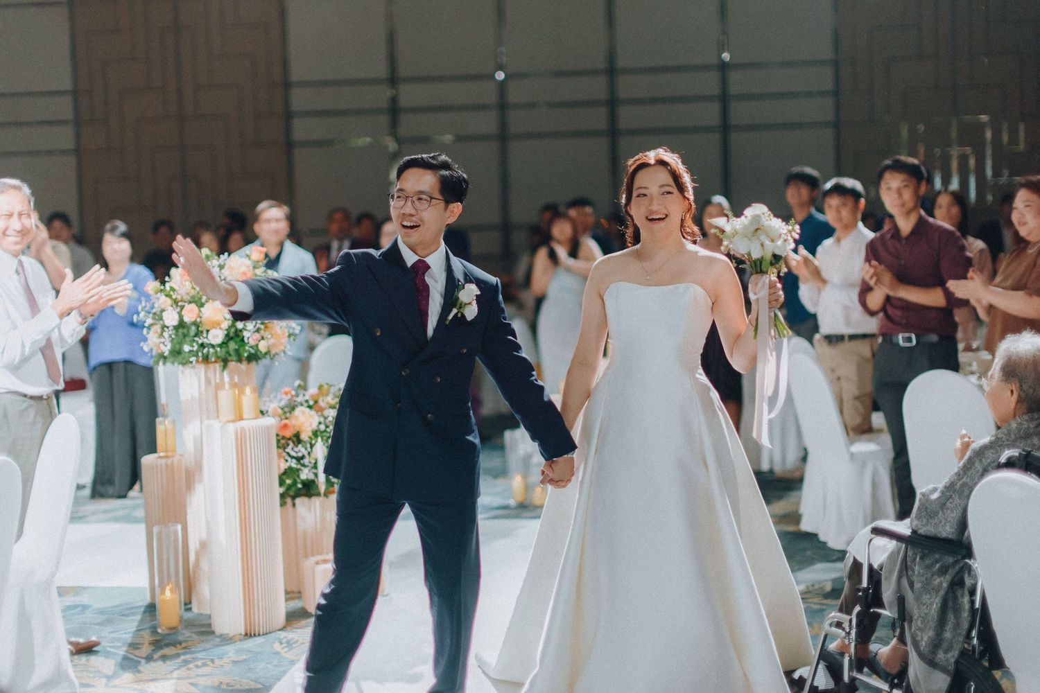 Newlyweds celebrating during their wedding ceremony with guests applauding in the background.