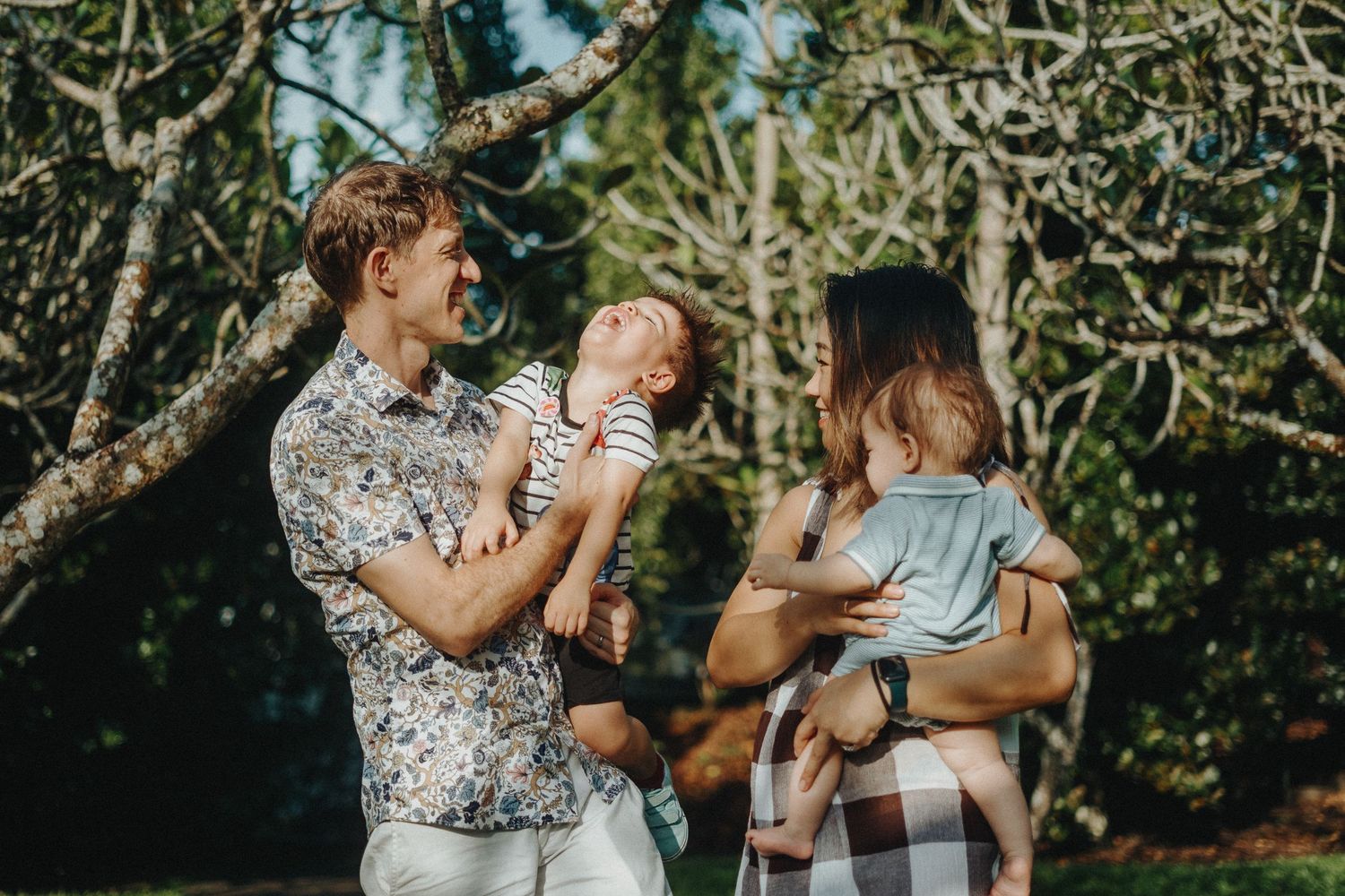 A family enjoys a sunny afternoon together outdoors among olive trees in a garden.