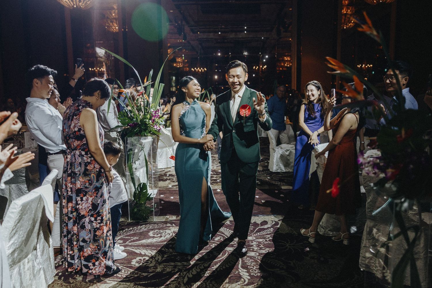 Guests mingle and celebrate at an elegant evening wedding reception with floral arrangements and moody lighting.