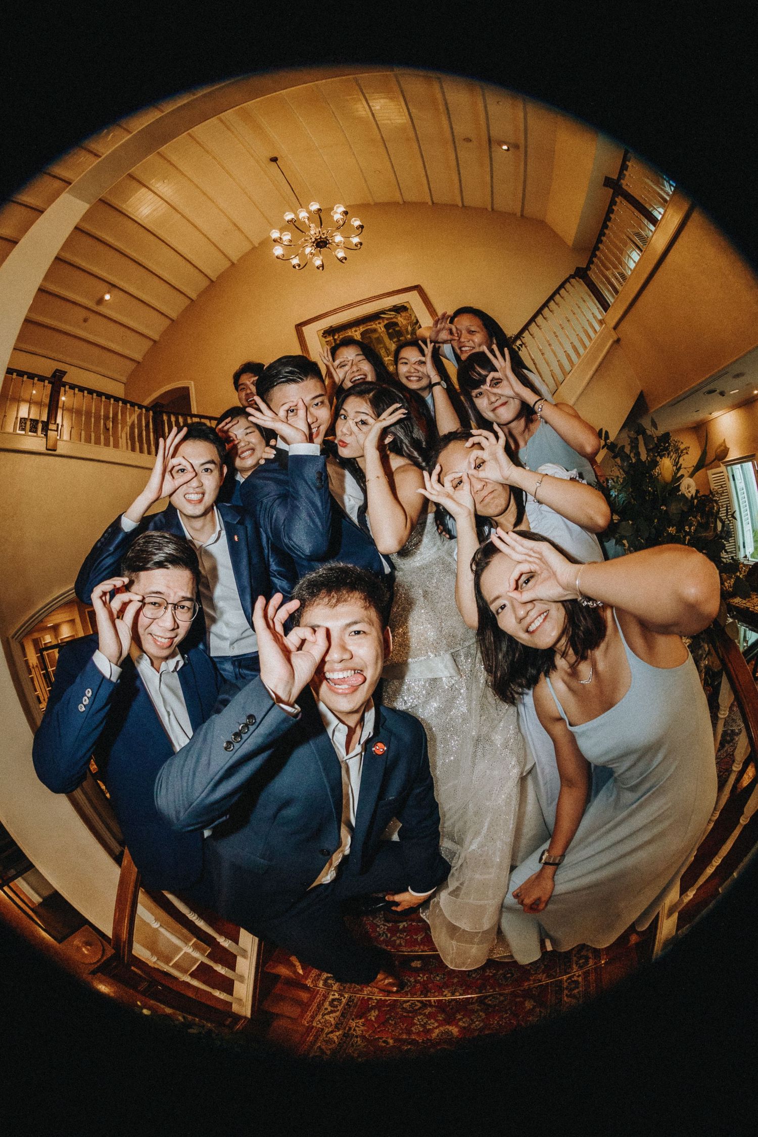 Fun fisheye lens photos of wedding party making silly faces and poses in warm-lit indoor venue.