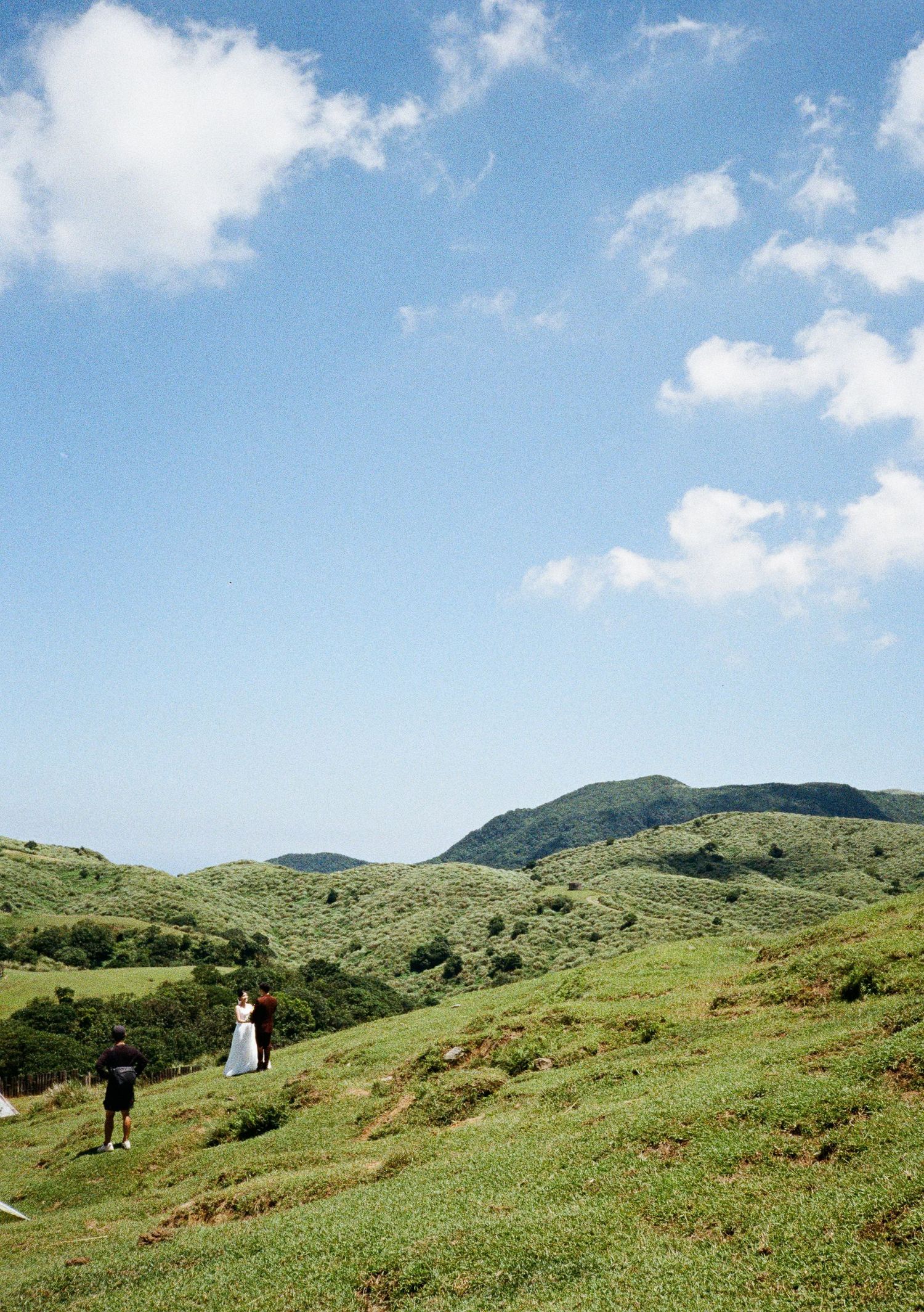 Rolling green hills with scattered people walking along the grassy slopes under blue skies.