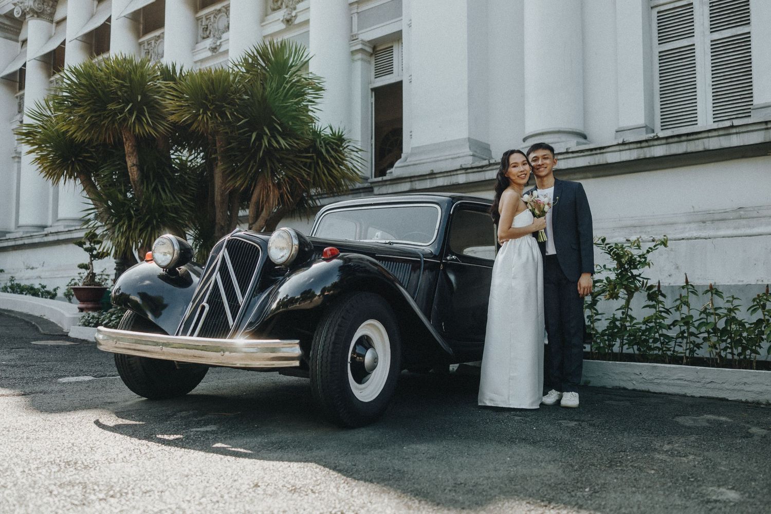 Elegant vintage car parked in front of white historic building with palm trees.