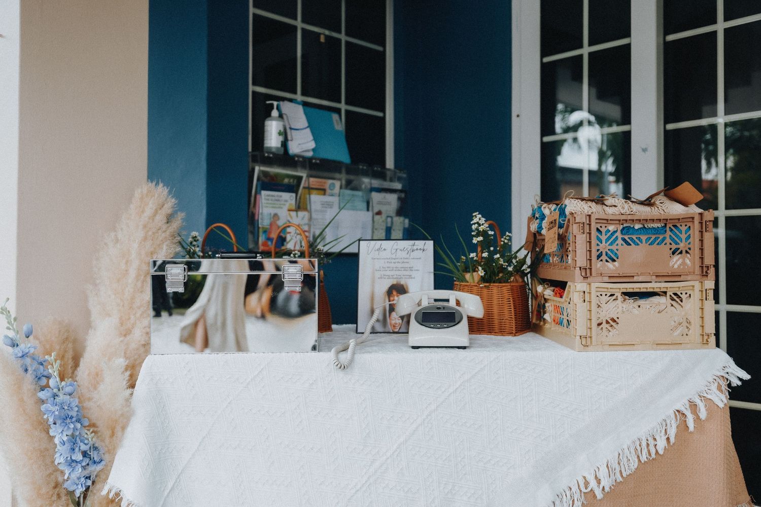A cozy display table with vintage decor, woven baskets, and pampas grass against a navy blue wall.