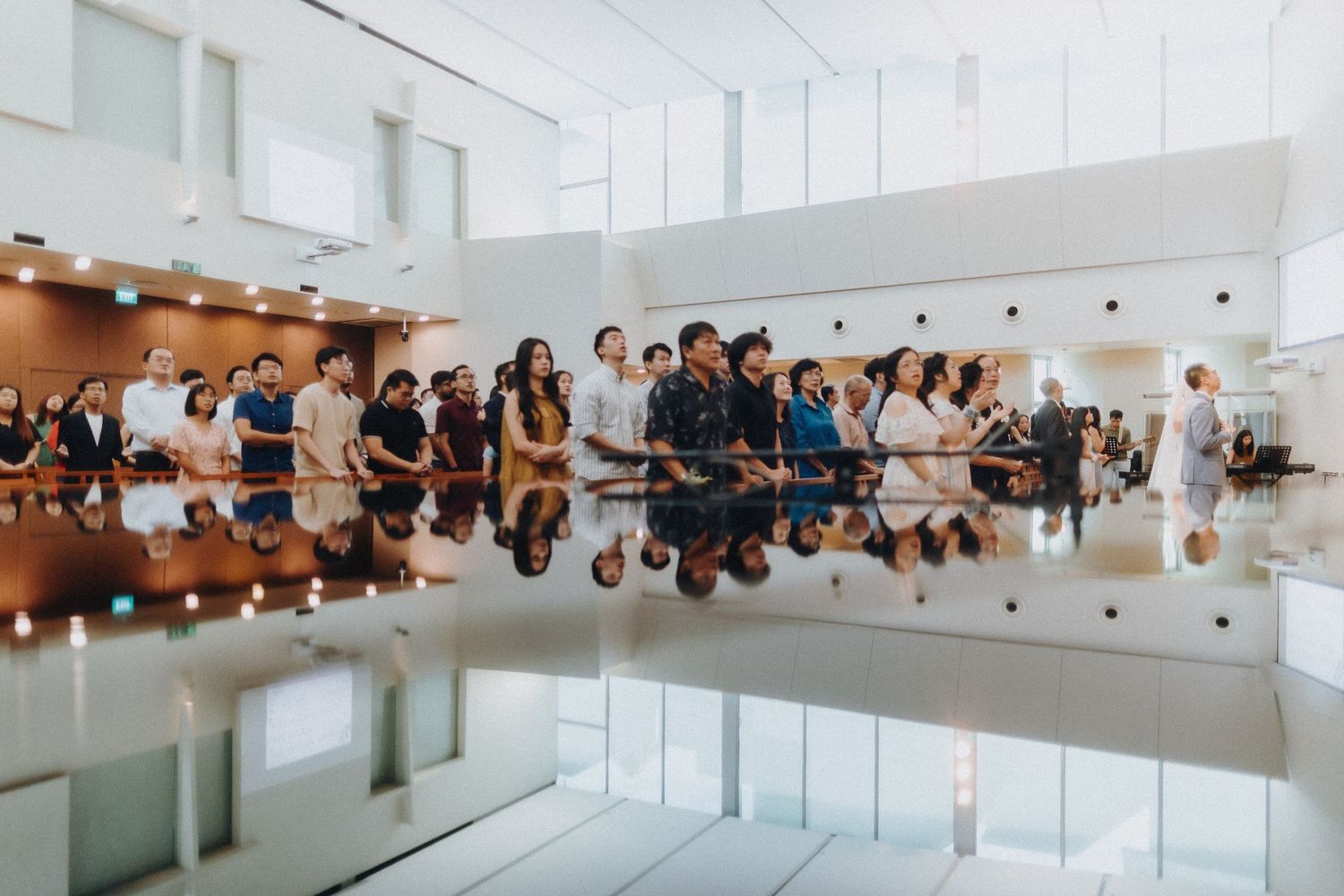 Modern white venue with glass railings and large windows overlooking guests at an event.