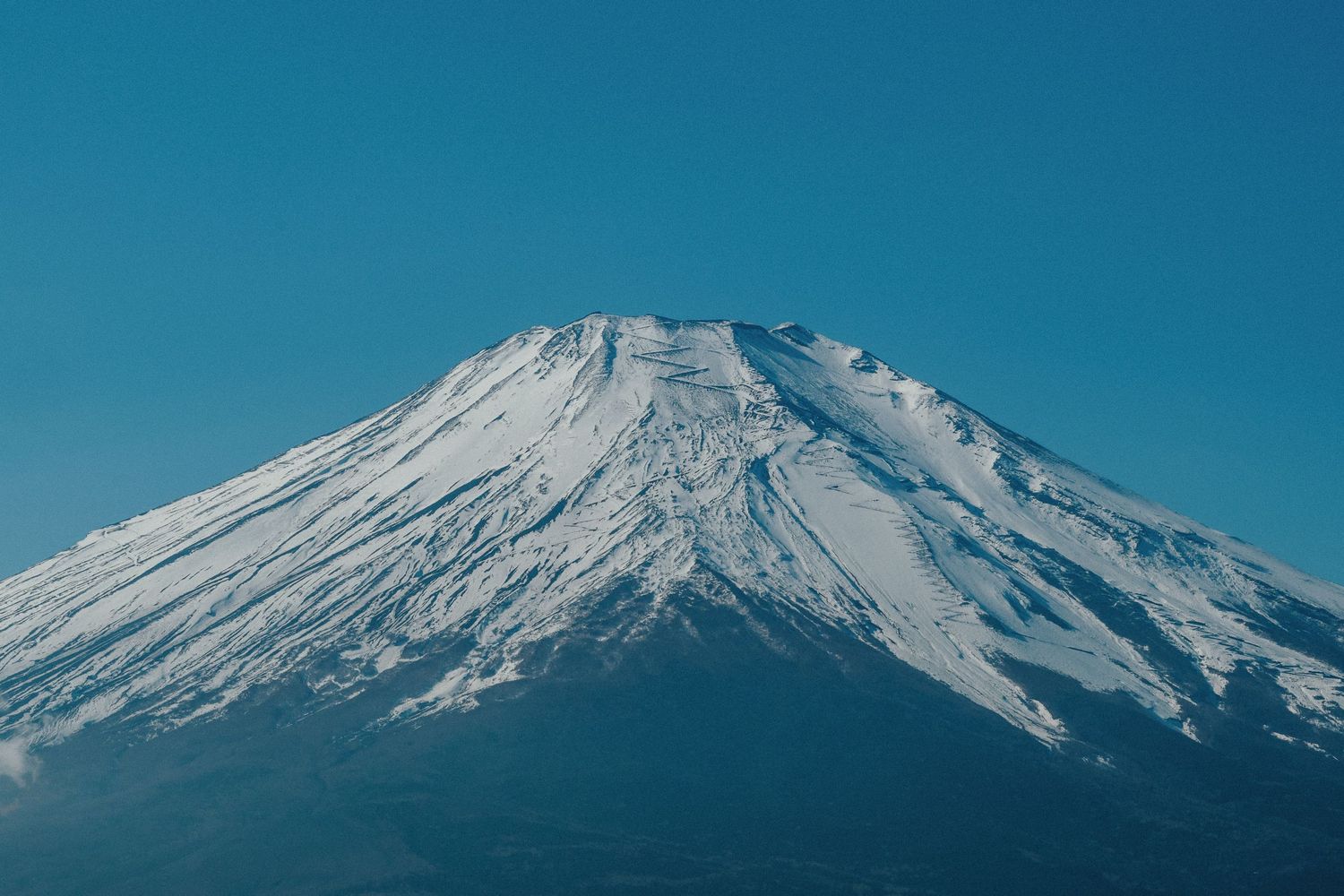 Panoramic view of snow-covered Mount Fuji against a vibrant blue sky.