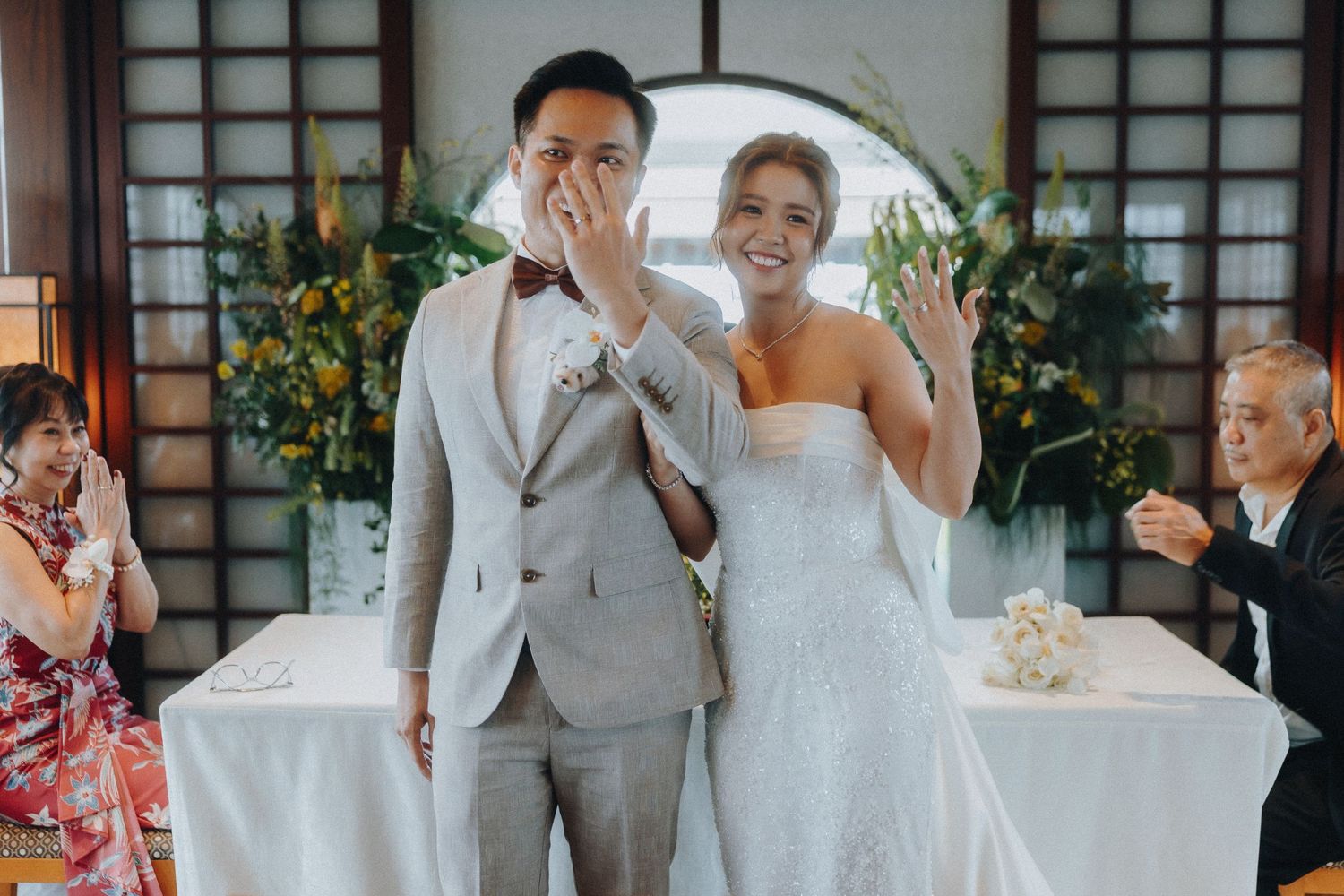Wedding ceremony guests and couple gather in traditional Japanese room with natural lighting.
