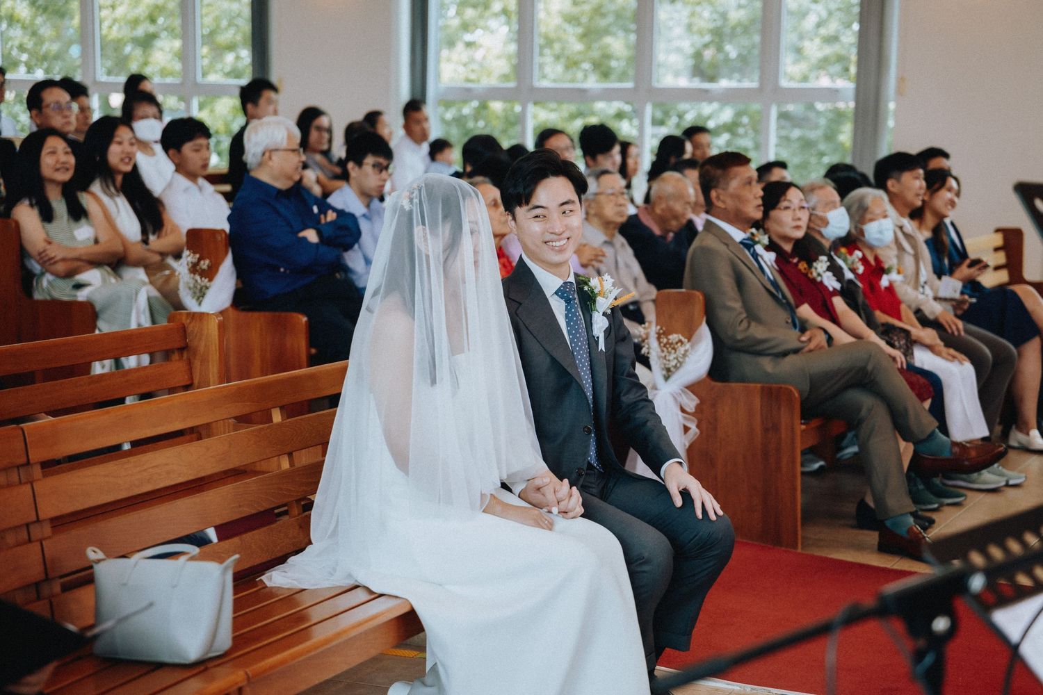 Bride in veil and groom sit together smiling during wedding ceremony in a sunlit church.