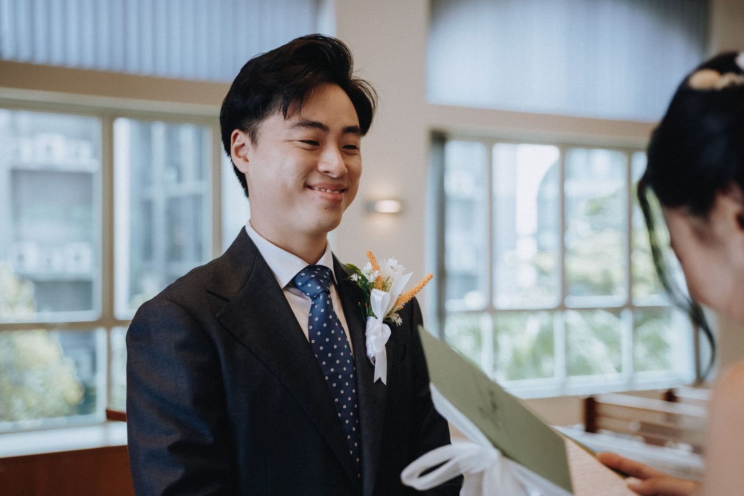 Smiling groom in dark suit with floral boutonniere at wedding ceremony.