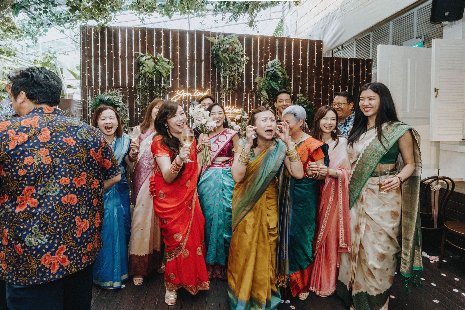 Group of women in colorful sarees laughing and celebrating at an Indian wedding reception.