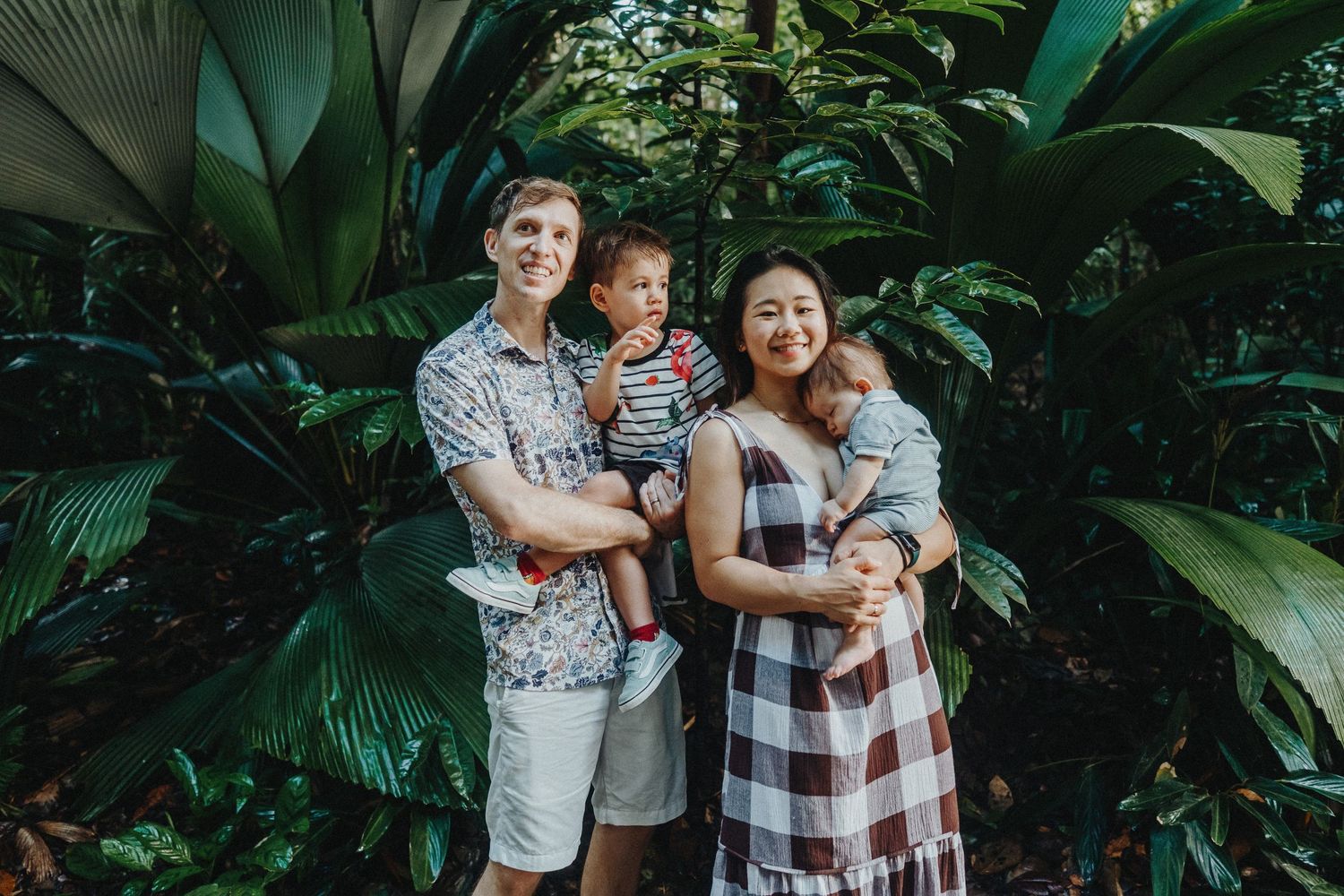 Family poses together in a lush tropical garden setting during outdoor photo session.