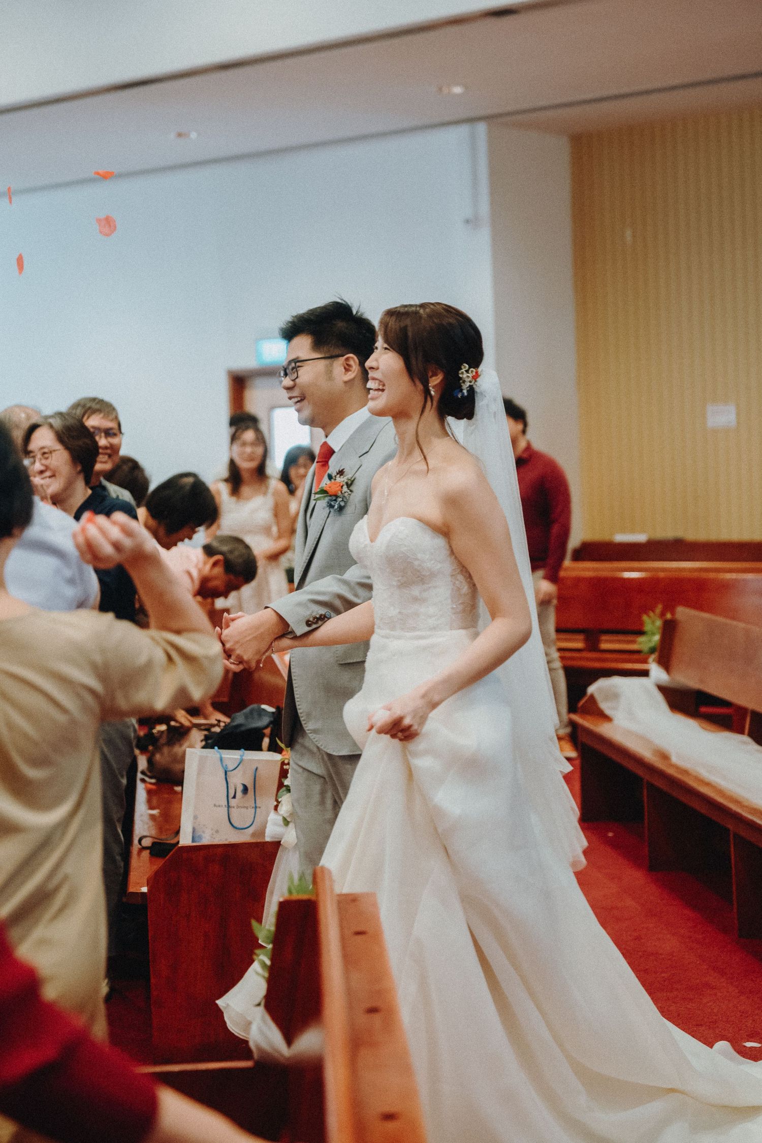 Couple in wedding attire greets guests in church aisle during celebration.