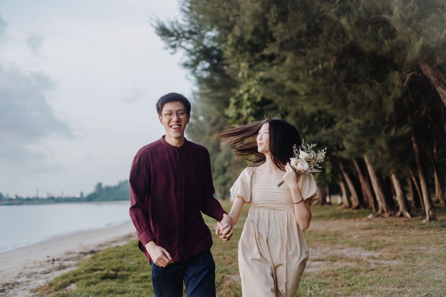 A couple walks together along a scenic beach path through palm trees and tropical vegetation during an engagement session.