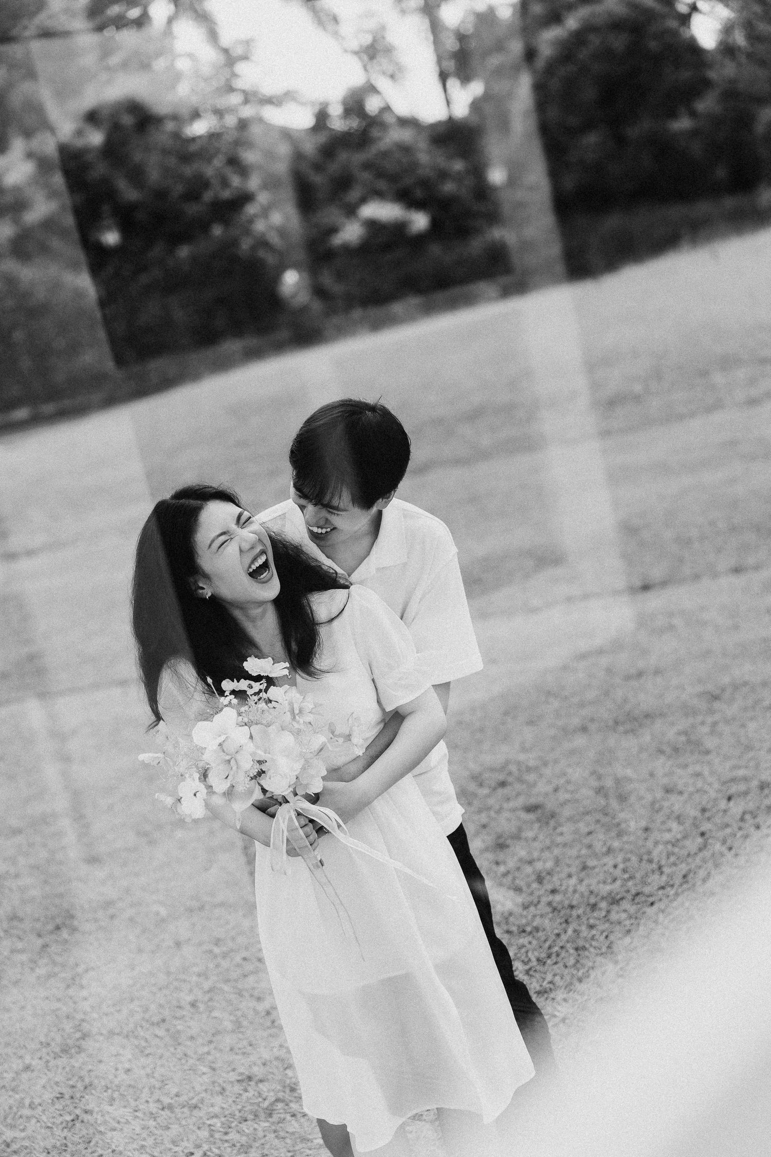 Couple sharing joyful moment with bouquet in outdoor garden setting.
