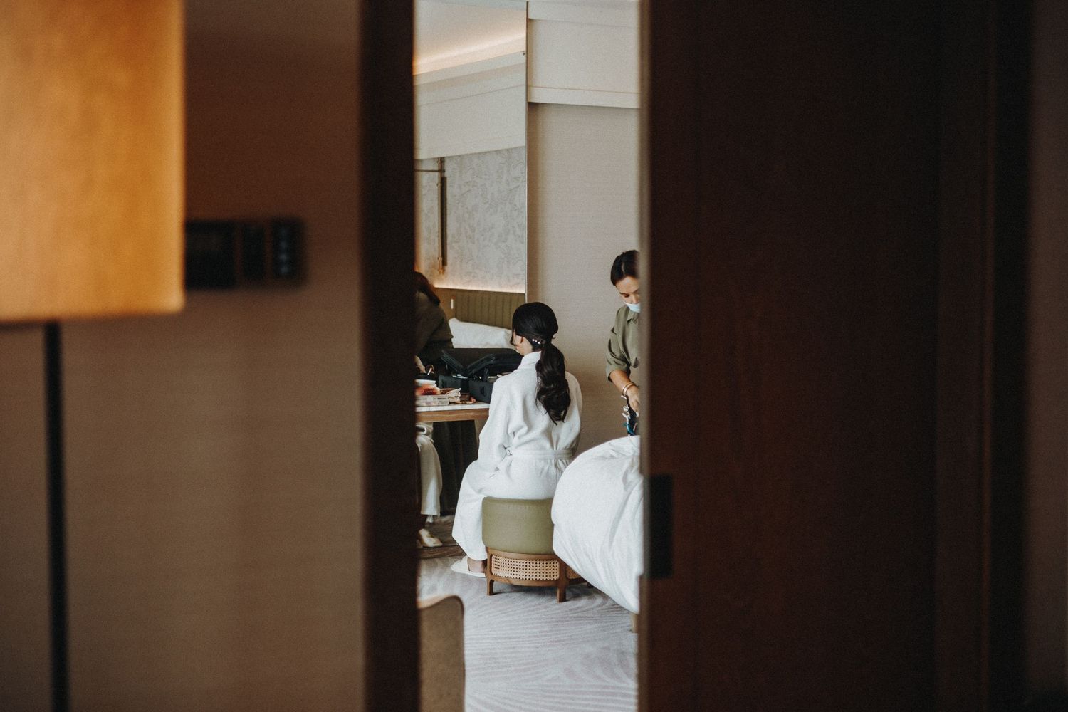 A glimpse through a doorway into a wedding preparation scene with flowing white dress fabric in a softly lit room.