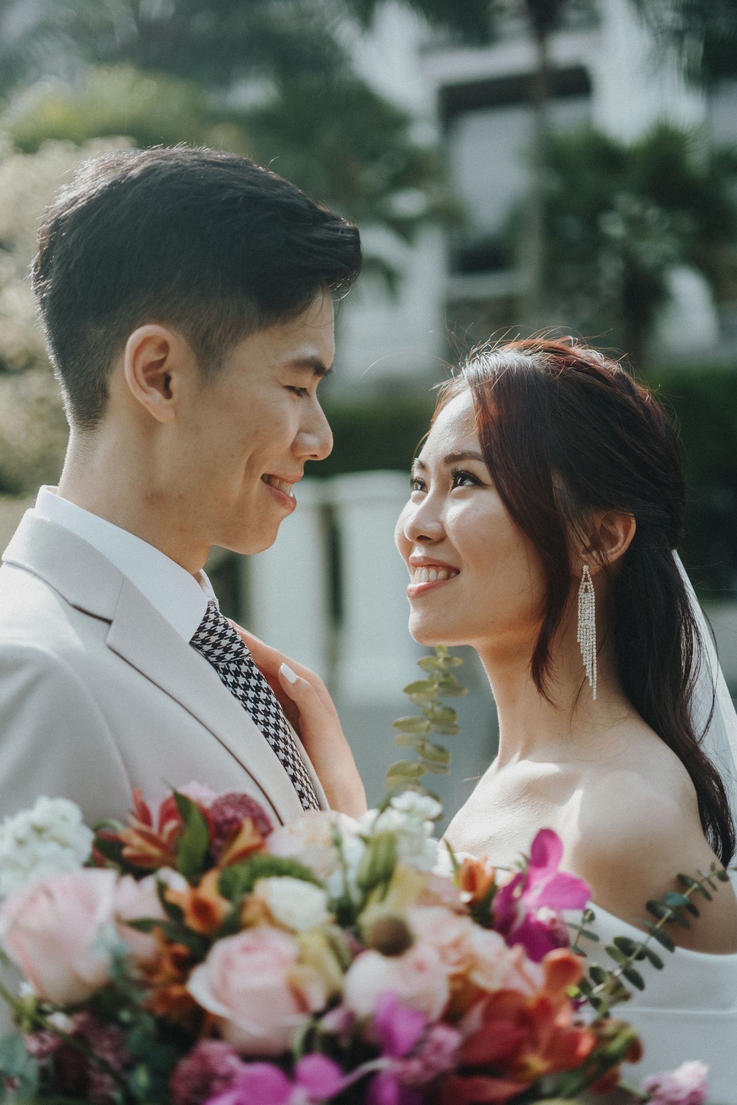 A romantic wedding portrait features a couple with a vibrant pink and white floral bouquet.