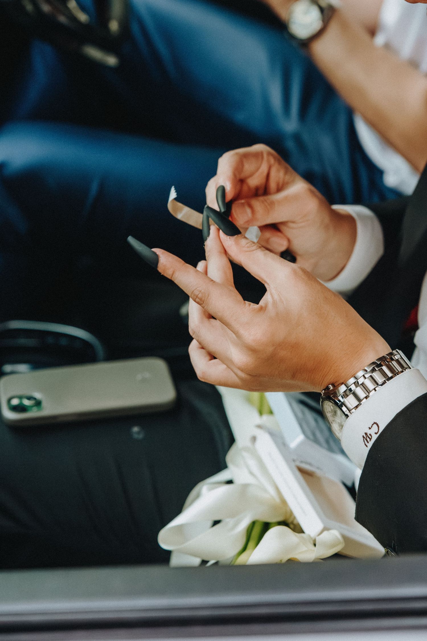 Close-up view of hands holding mobile phones at a formal event with white floral decorations in background.