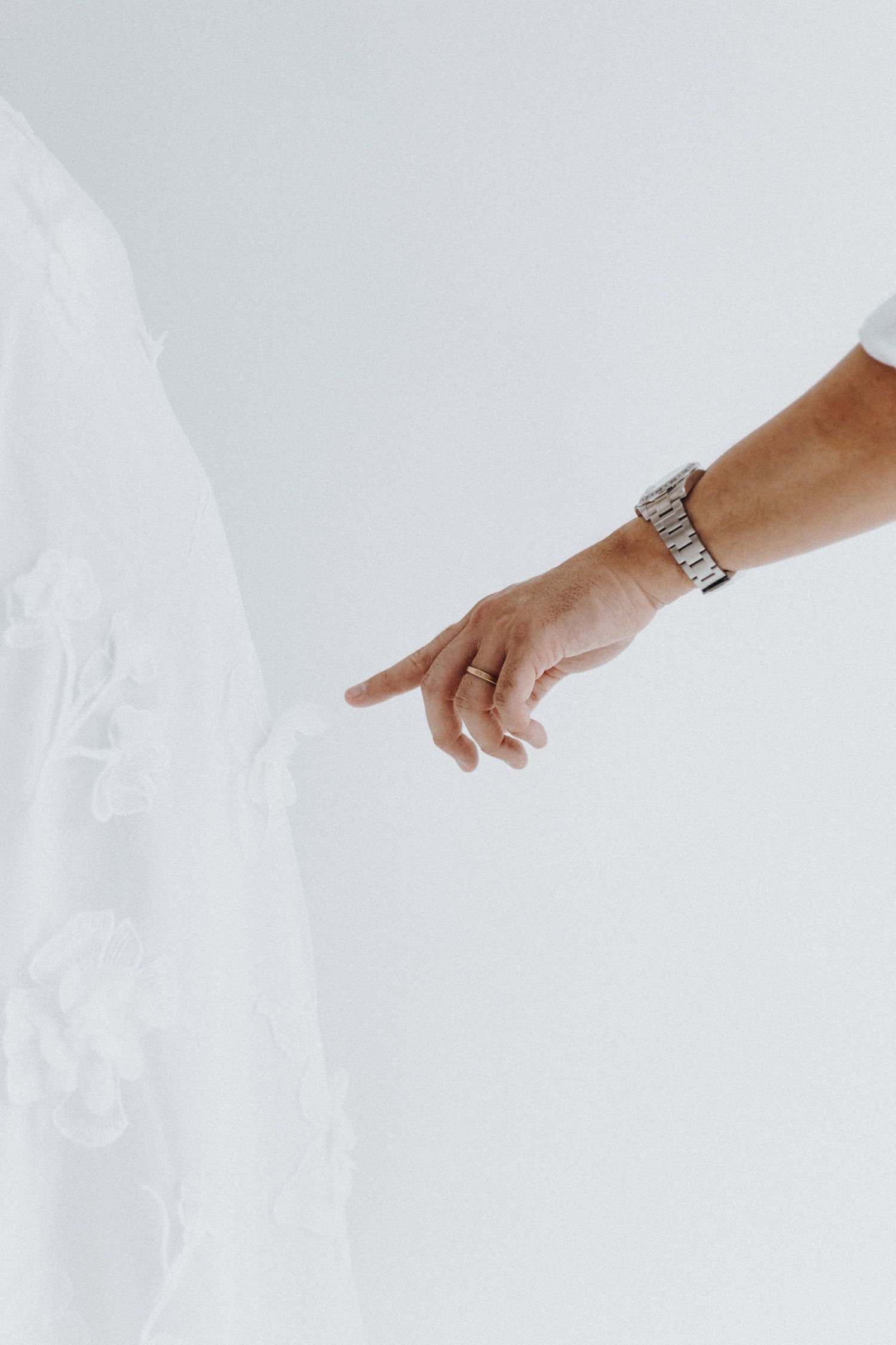 Close-up of a hand wearing a silver watch reaching towards white fabric in a minimalist setting.