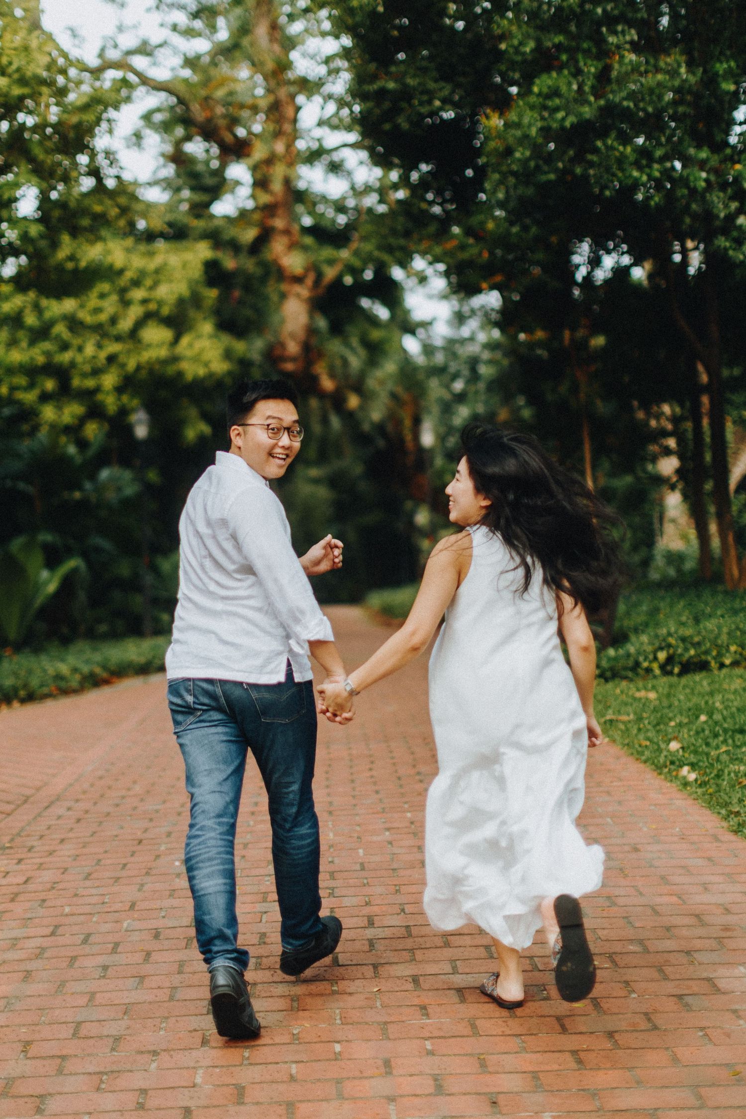 Couple walking and running playfully on a brick pathway surrounded by lush greenery.