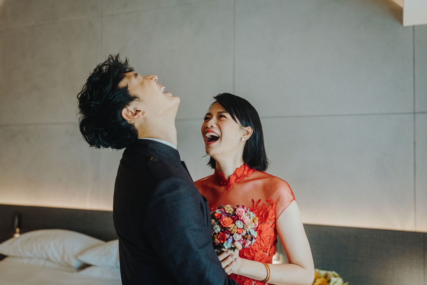 Couple laughing together with person in red traditional dress holding flowers.