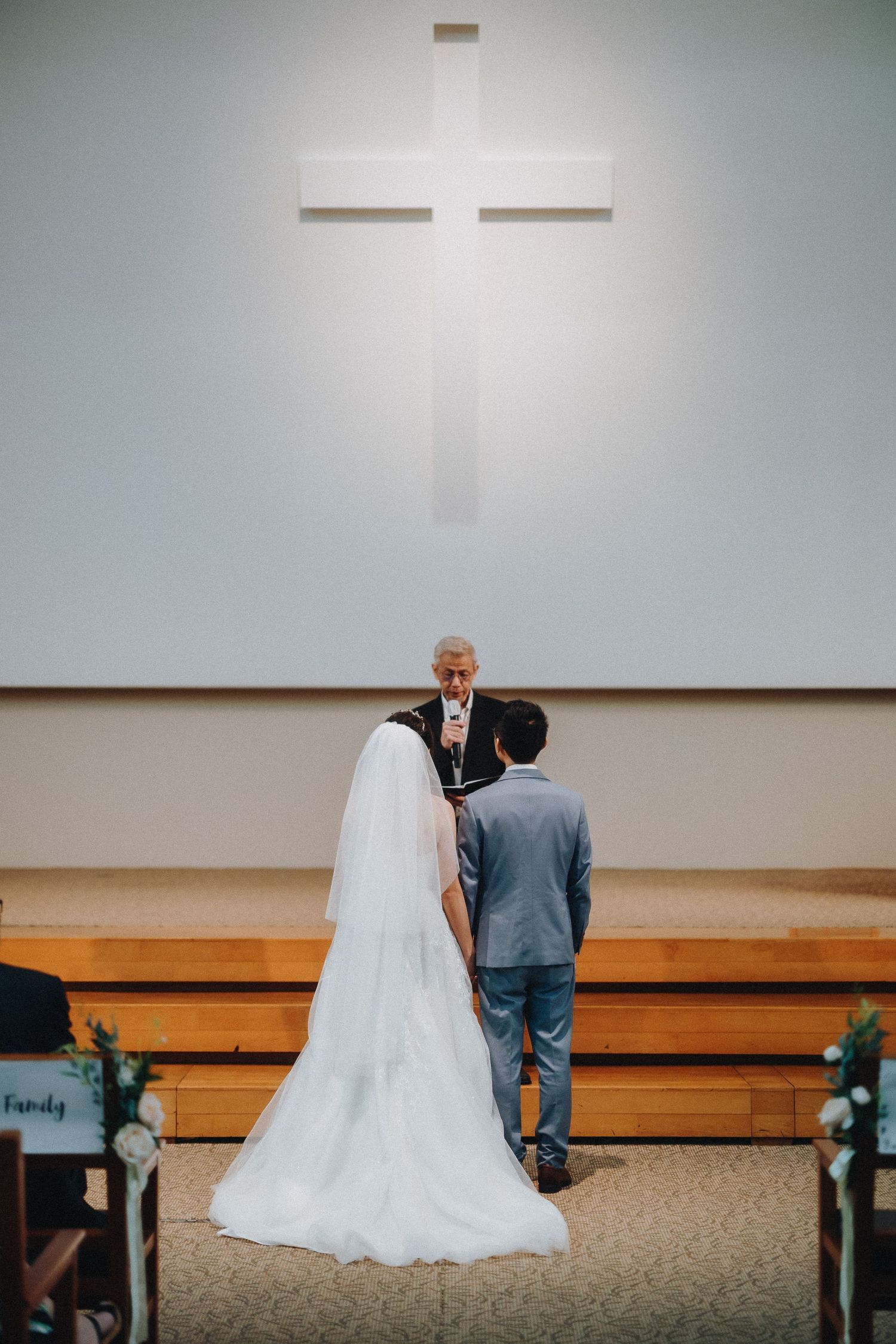 A church ceremony with a wooden cross on white wall and chairs arranged in rows facing the altar.