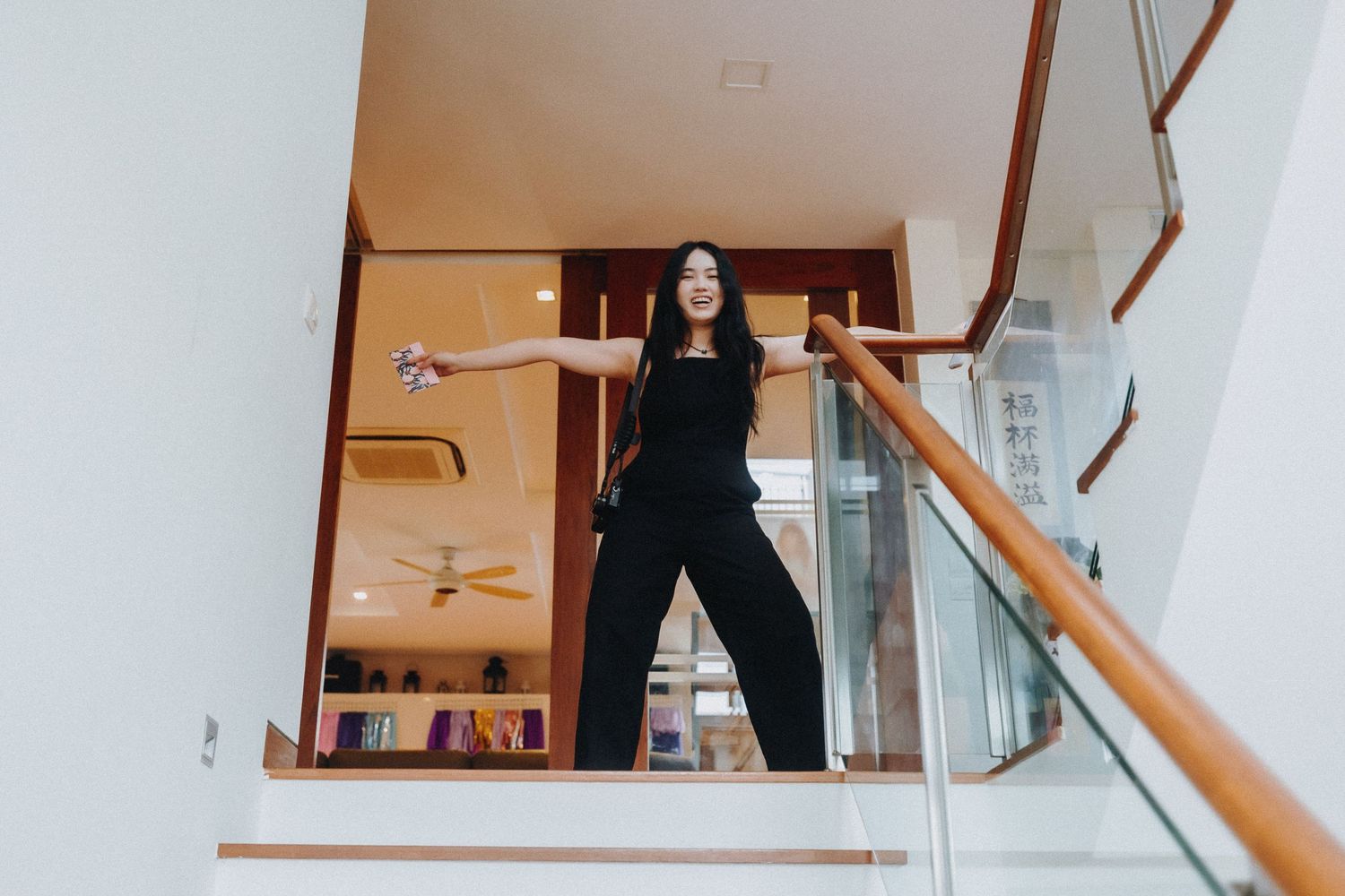 A person in all black poses confidently on a staircase landing with arms spread wide.