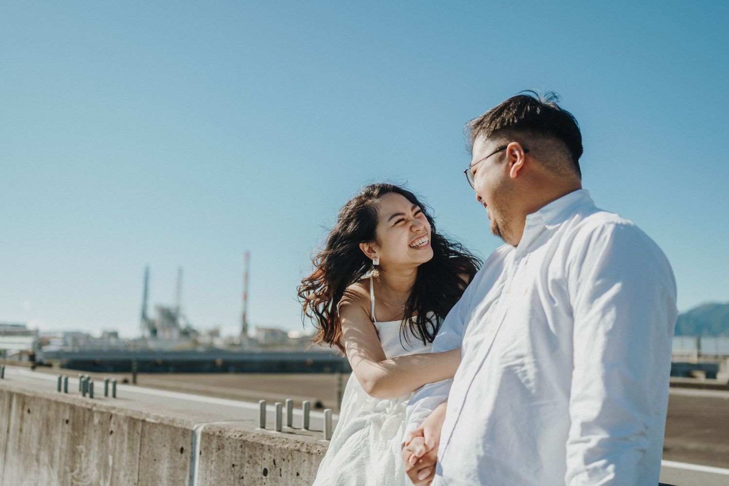 A couple embraces on a sunny beach with ocean waves in the background.