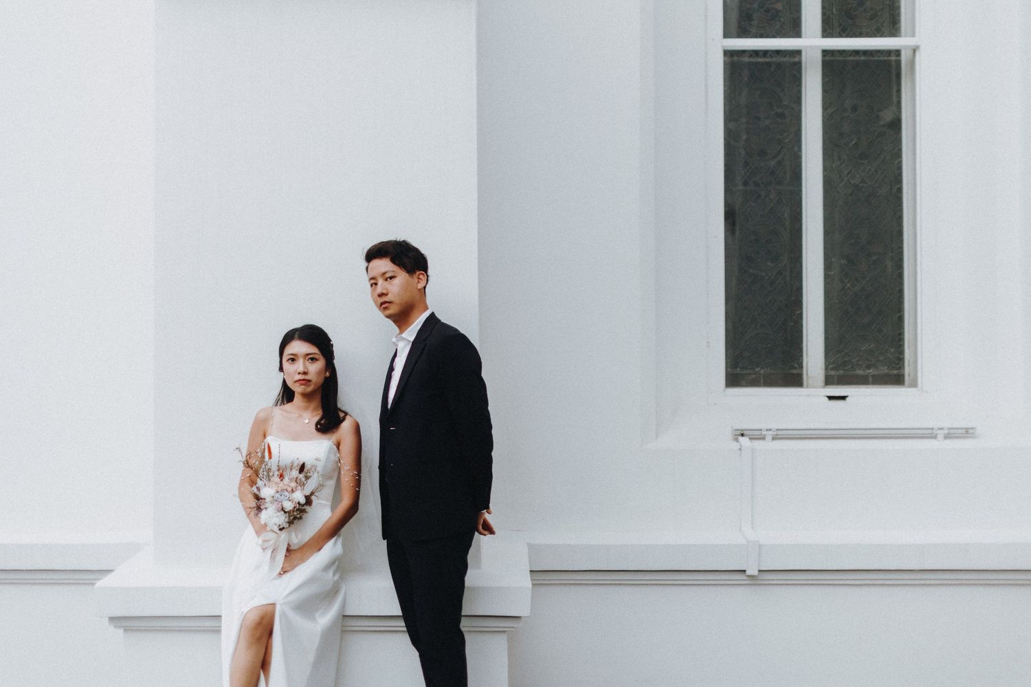 Elegant wedding portrait against white architectural backdrop.