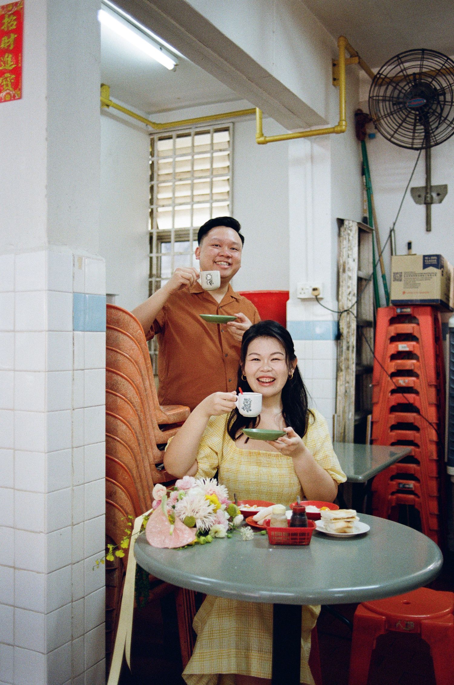A couple enjoys drinks together at a casual eatery with white tiled walls and red plastic chairs.