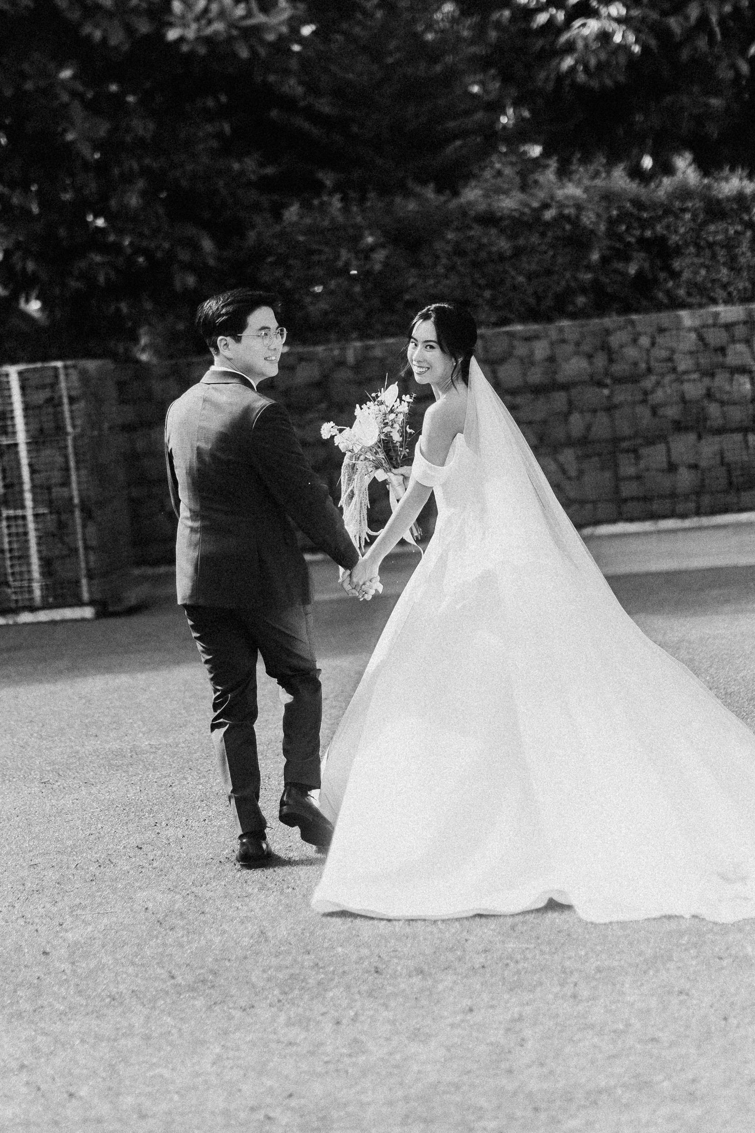 Black and white wedding photo of newlyweds sharing a romantic moment outdoors by a stone wall.
