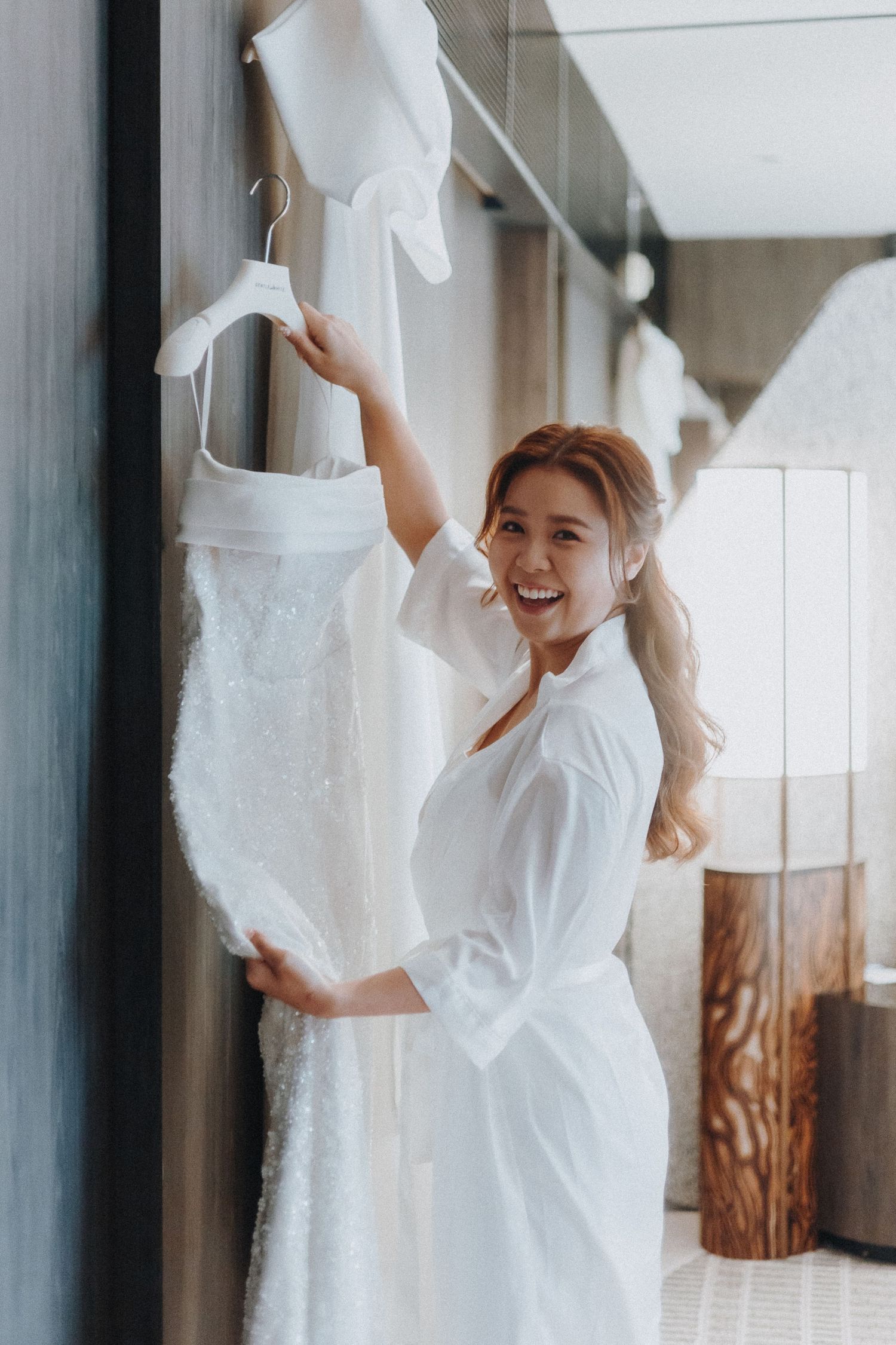 Wedding dress preparation in a bright room with white robe and hanging gown.
