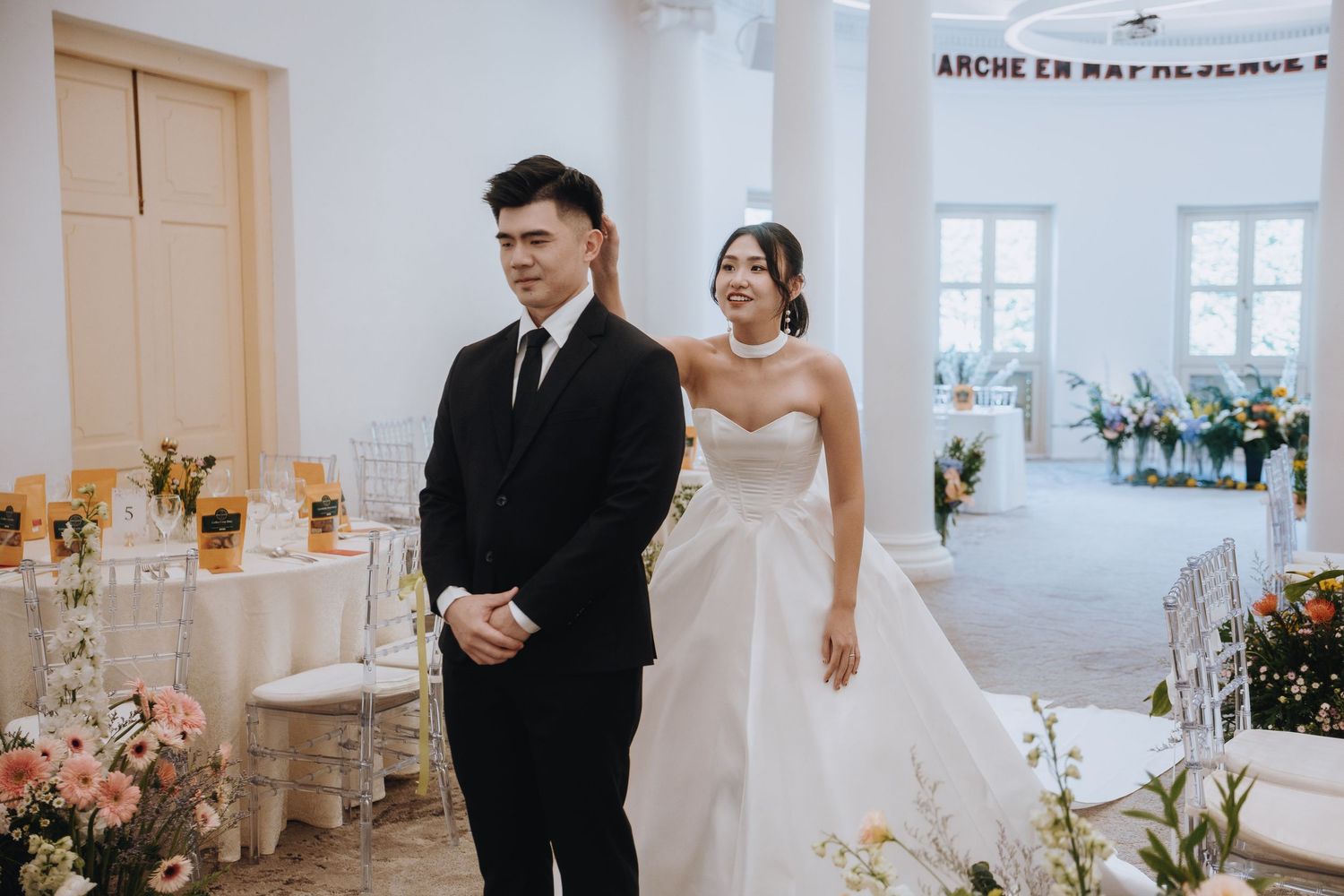 Bride in white gown and groom in black suit stand together during wedding ceremony.